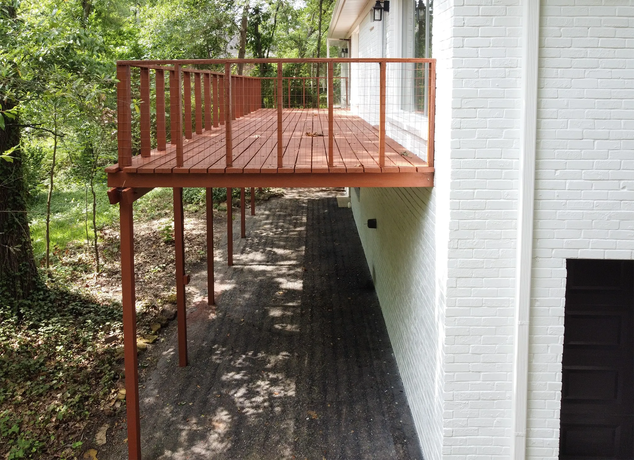 Elevated wooden deck featuring a railing, white painted brick exterior, and a lower-level paved patio area