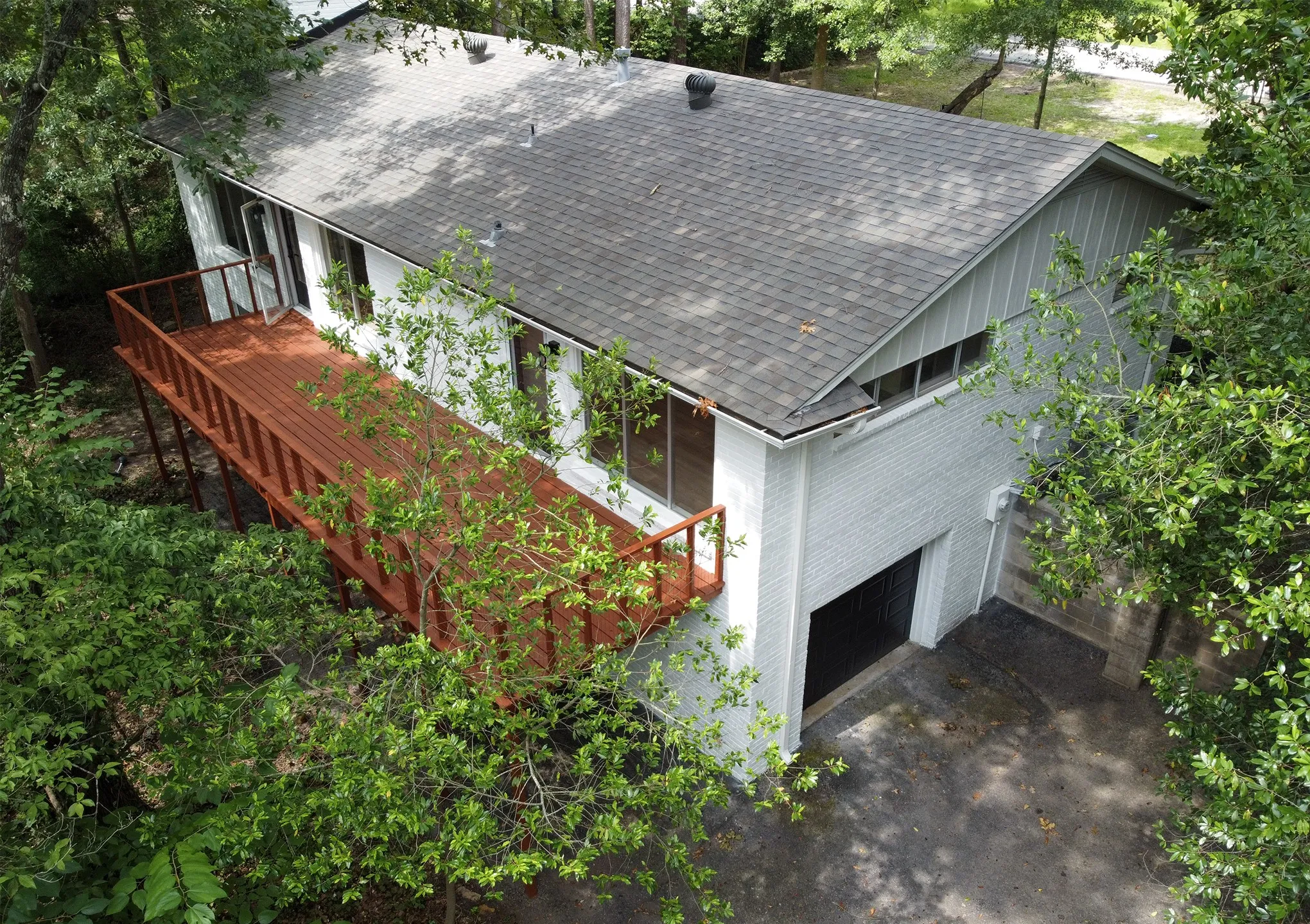 White brick exterior featuring an expansive wood deck, asphalt shingle roof, vertical siding accents, and a ground-level garage
