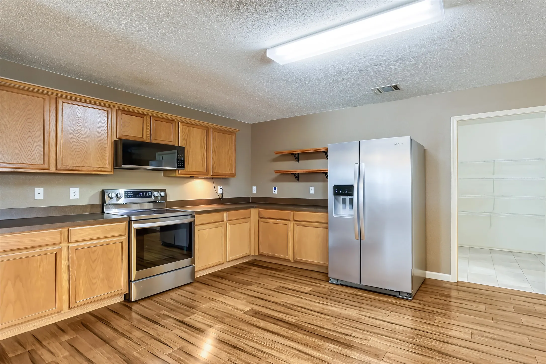 Kitchen featuring wood-finish cabinetry, stainless steel appliances, open shelving, and wood-finish flooring