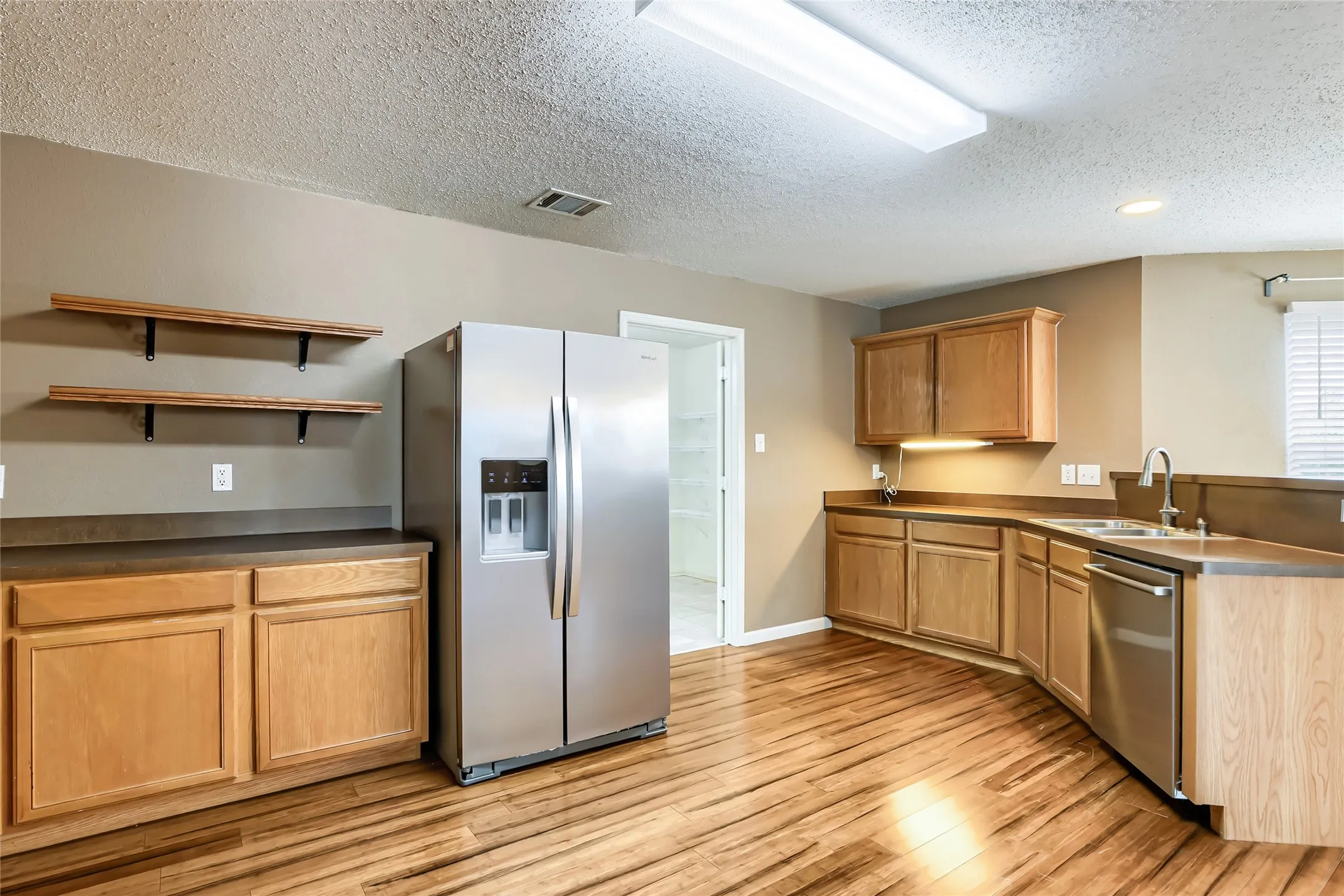 Kitchen featuring wood-finish cabinetry, stainless steel appliances, wood-finish flooring, solid-surface countertops, and open wood shelving