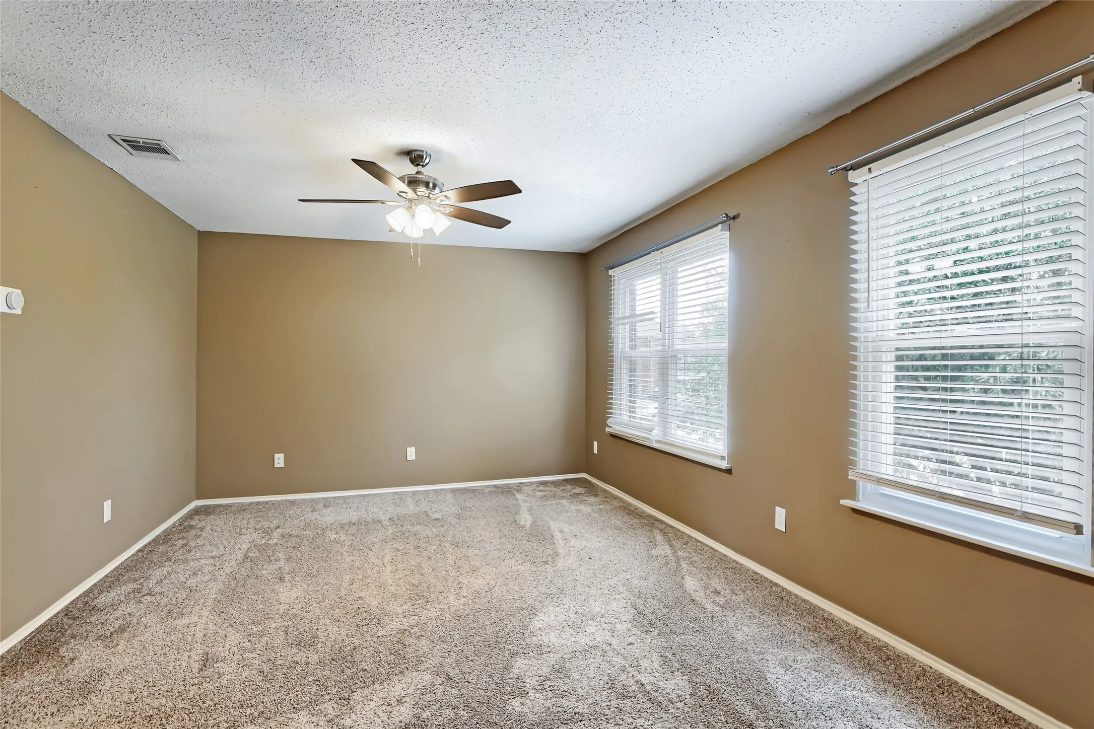 Room featuring wall-to-wall carpeting, neutral-toned walls, windows with horizontal blinds, and a multi-blade ceiling fan with integrated lighting