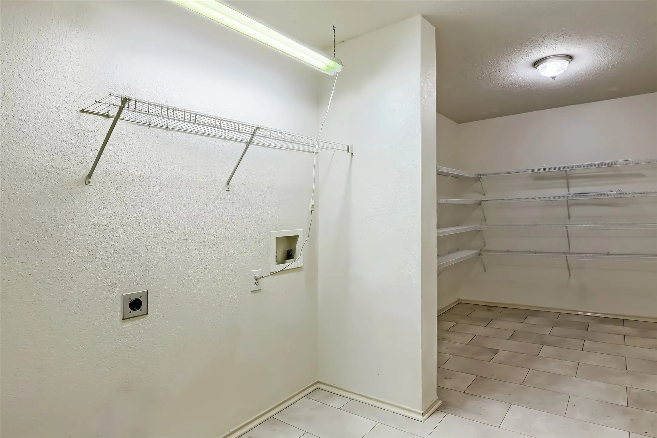 Utility area featuring tile flooring, ceiling-mounted lighting, and extensive wall-mounted wire shelving