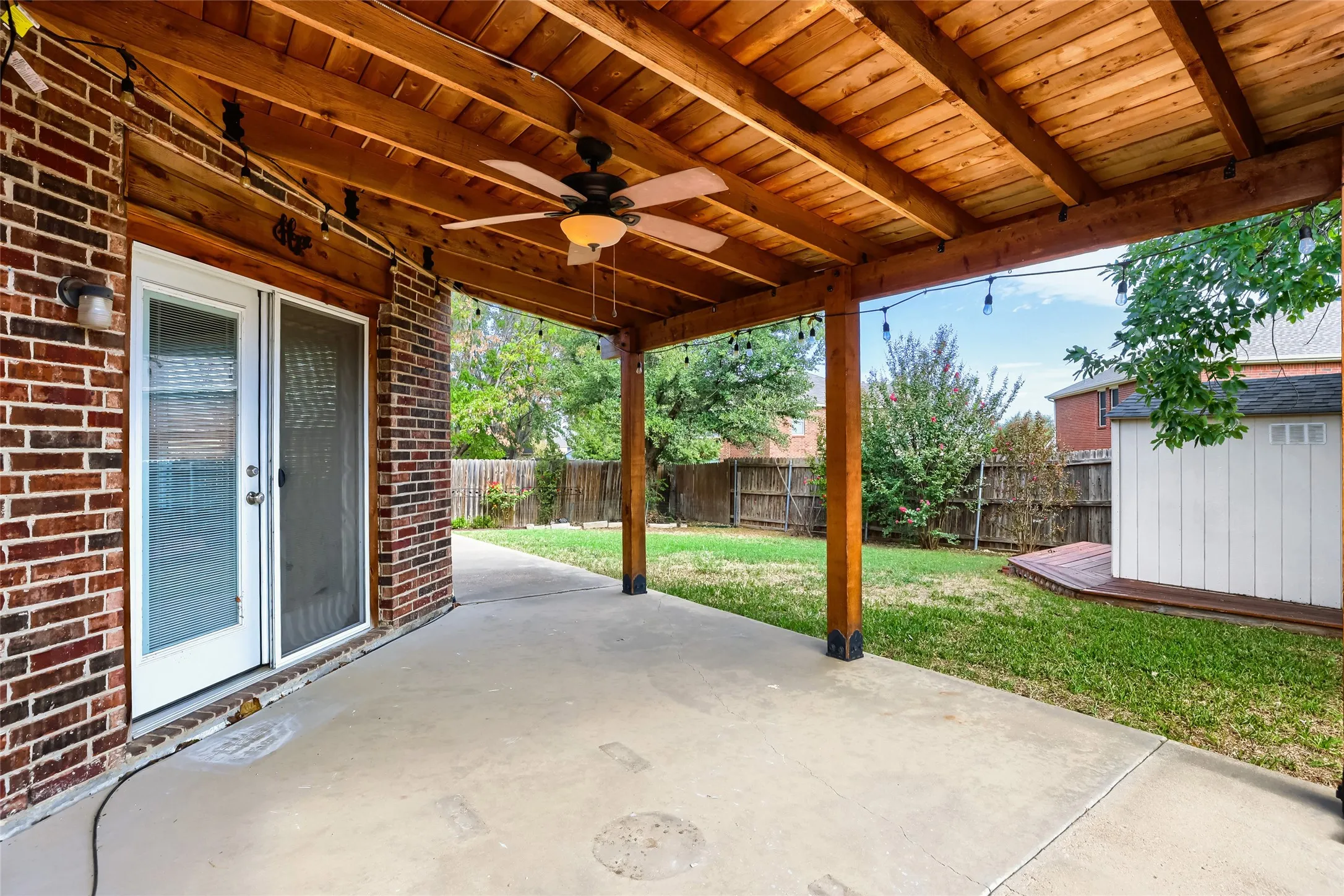 Covered patio featuring a wood-plank ceiling, exposed timber framing, a ceiling fan, concrete flooring, and a brick exterior wall