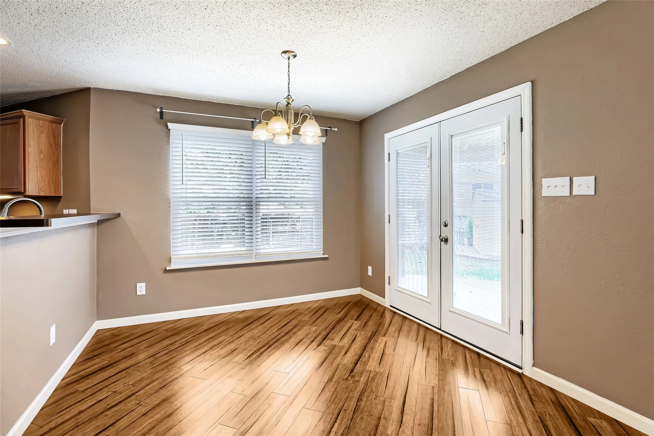 Wood-finish flooring, multi-light chandelier, double glass-panel doors, and horizontal window blinds