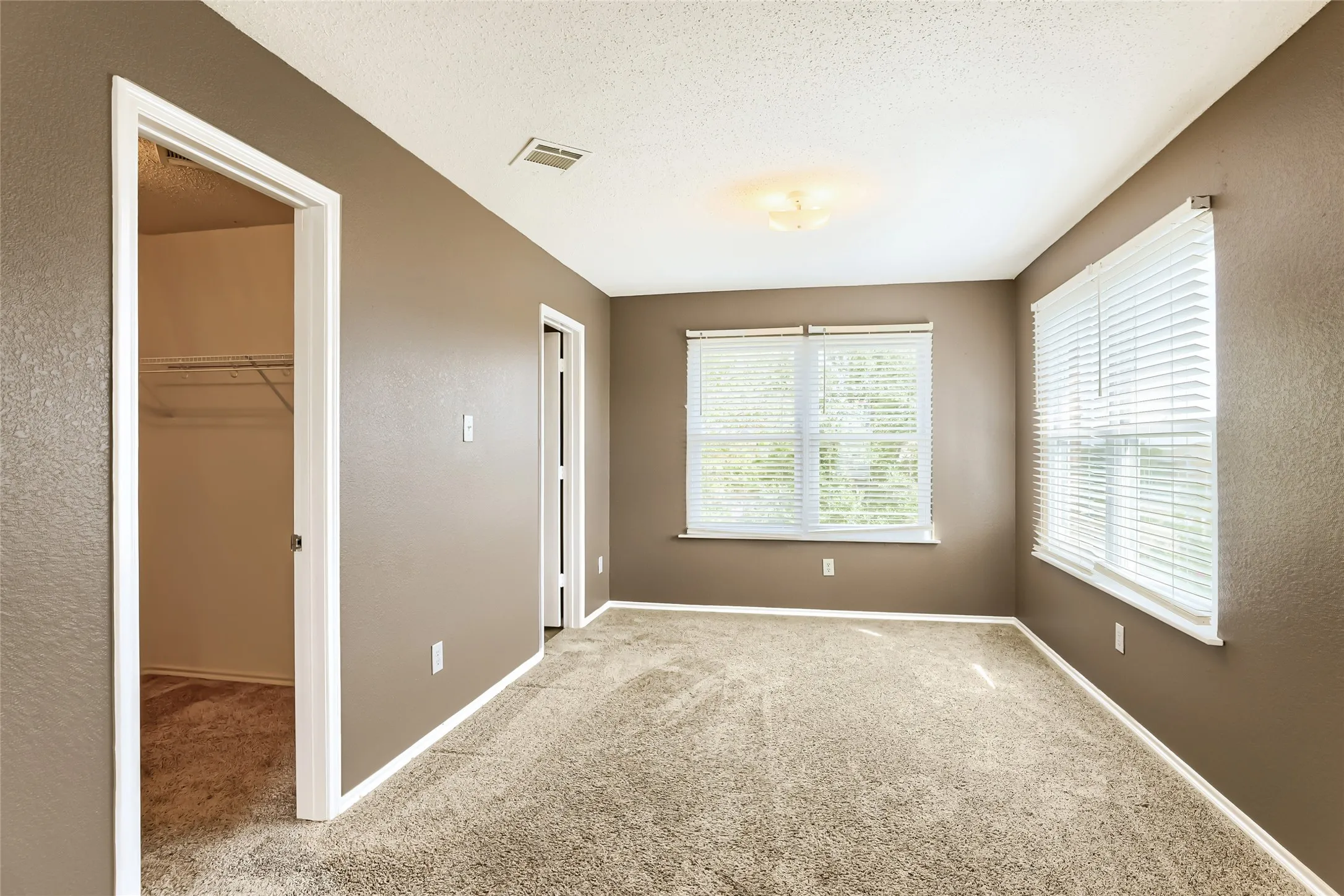 Interior room featuring neutral-tone walls, wall-to-wall carpeting, multiple windows with white blinds, and a built-in closet with wire shelving