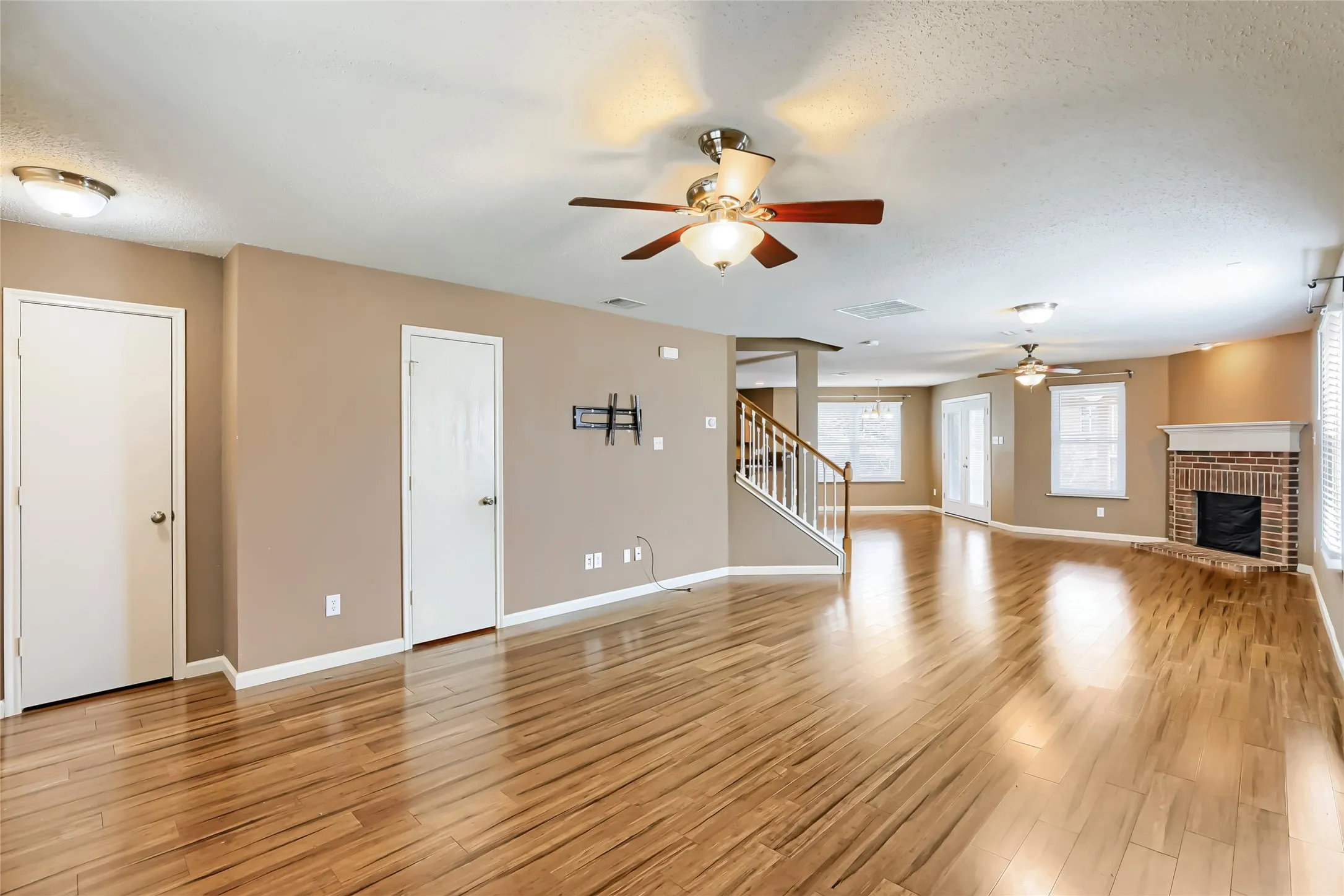 Open living area featuring wood-finish flooring, a brick fireplace, dual ceiling fans, and a staircase with wooden handrails