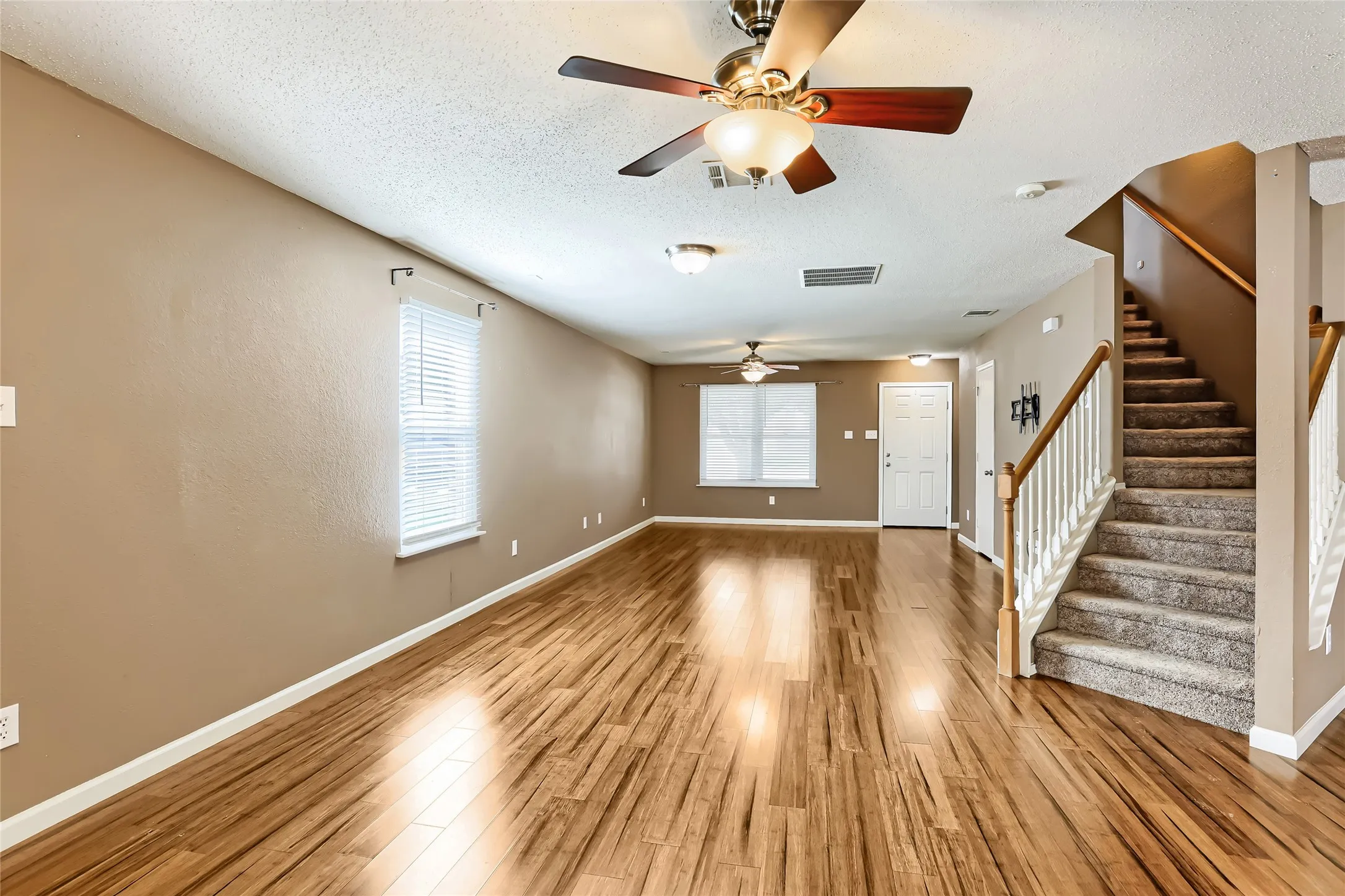 Open floor plan featuring wood-finish flooring, dual ceiling fans, and a staircase with white balusters and a wooden handrail