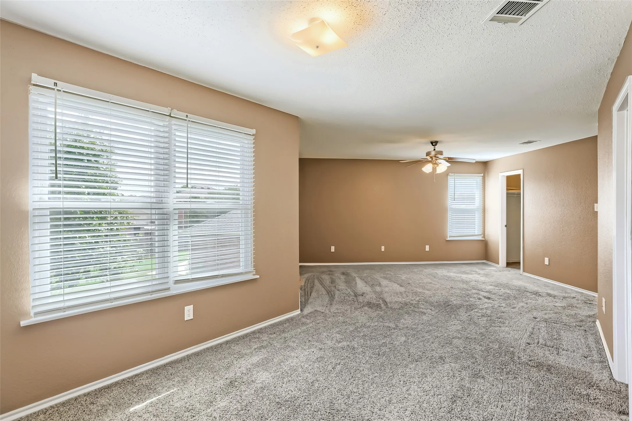 Room featuring wall-to-wall carpeting, multiple windows with horizontal blinds, a ceiling fan with light fixture, and square flush-mount overhead lighting