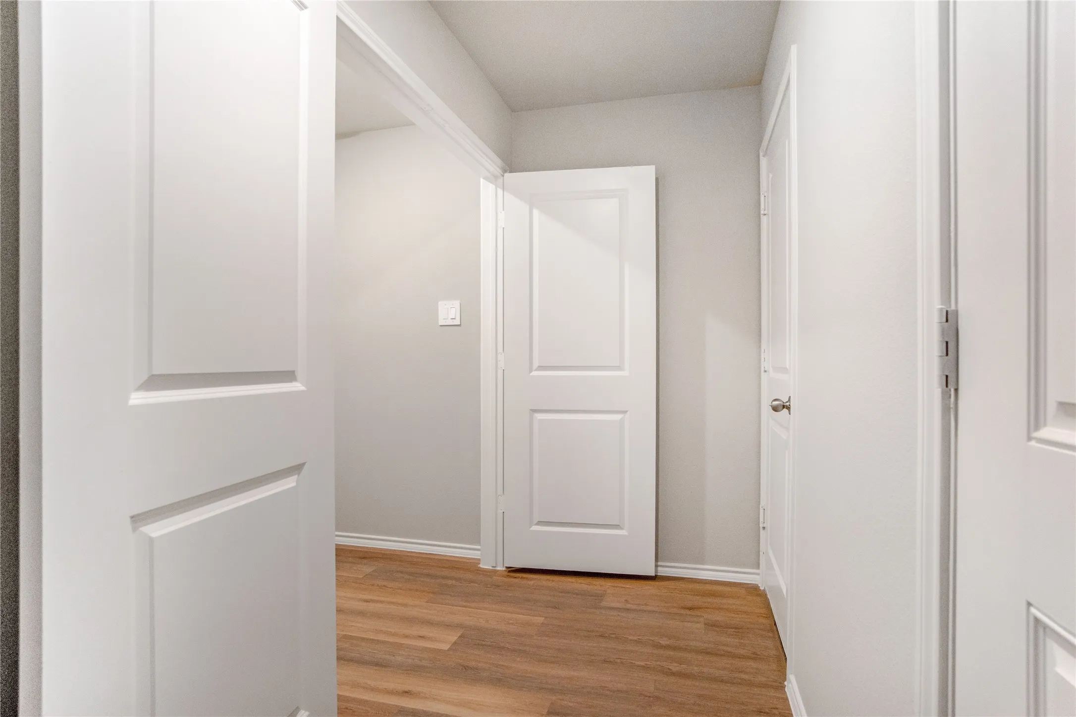 Hallway featuring wood-finish flooring, neutral walls, and multiple two-panel interior doors