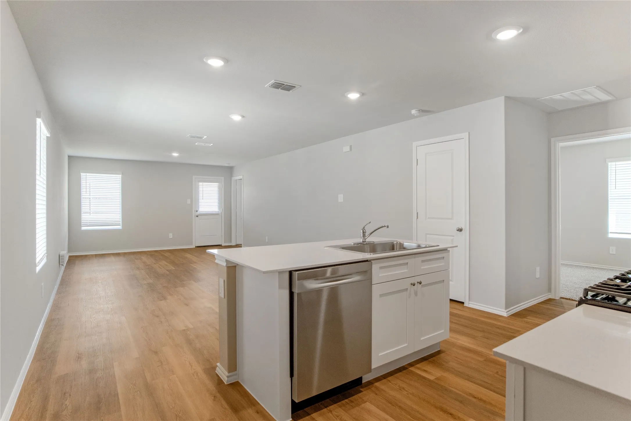 Kitchen featuring a central island with a stone-surface countertop, stainless steel sink with a gooseneck faucet, integrated stainless steel dishwasher, white cabinetry, and wood-finish flooring