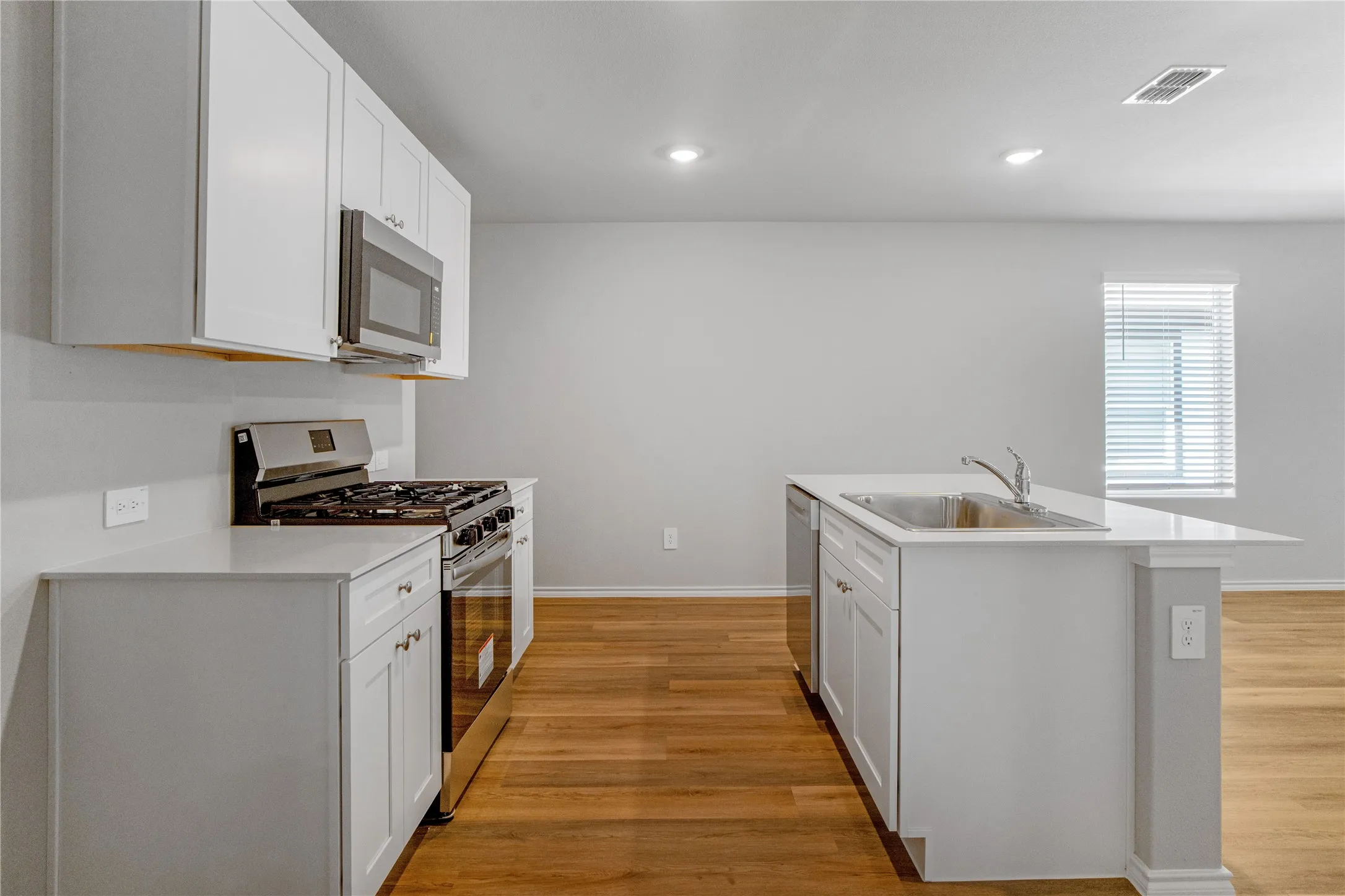Kitchen featuring white shaker-style cabinetry, quartz countertops, a central island with a stainless steel sink, stainless steel appliances, and wood-finish flooring