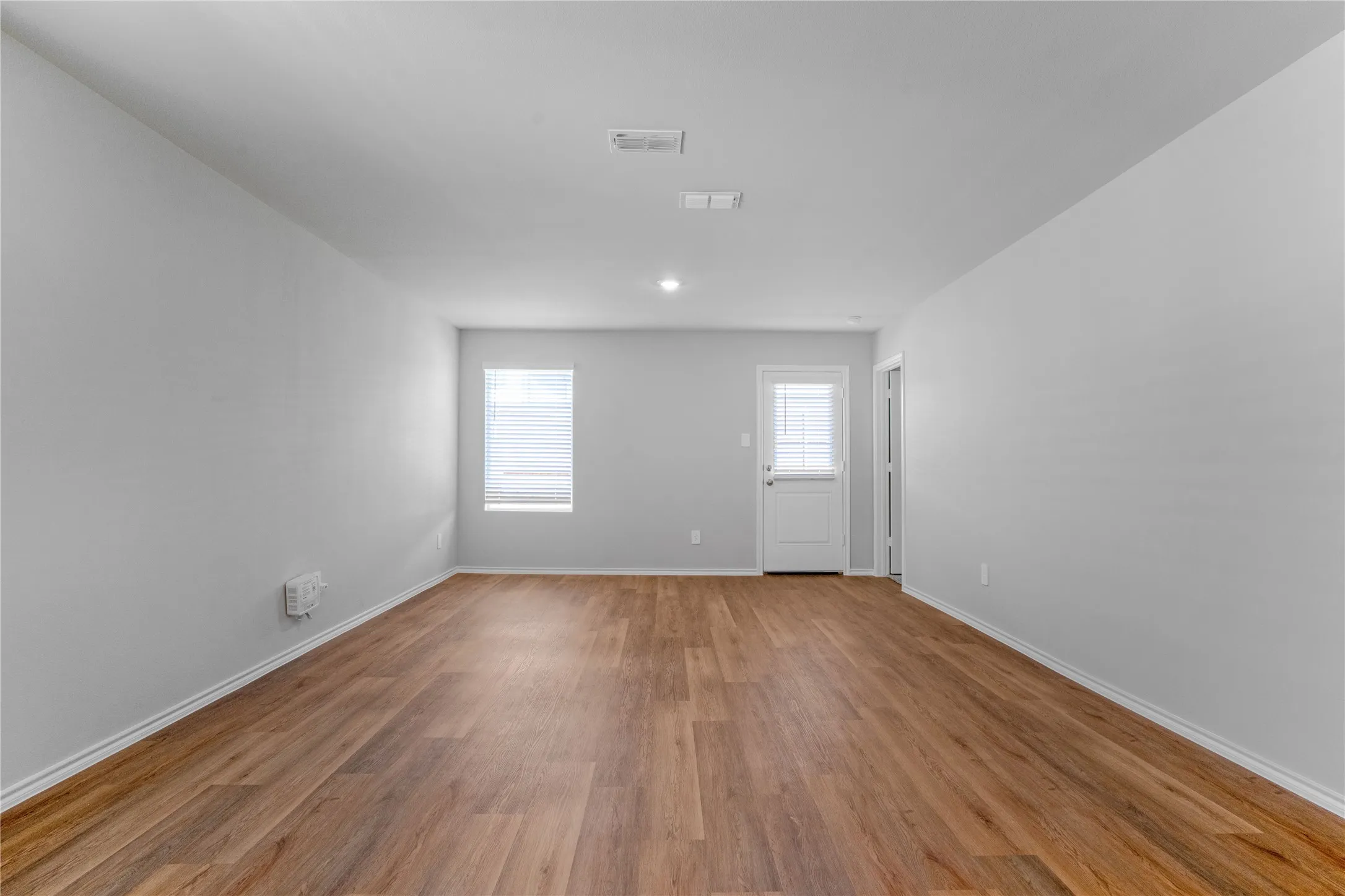 Neutral interior space featuring wood-finish flooring, recessed lighting, a single window, and a white exterior-access door