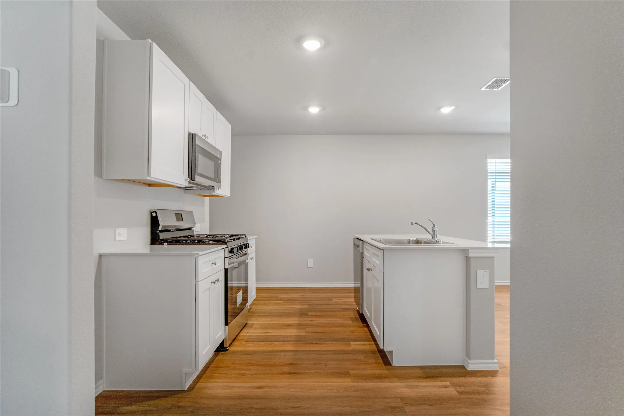 Kitchen featuring shaker-style white cabinetry, wood-finish flooring, a central island with an undermount sink, stainless steel gas range, and recessed lighting