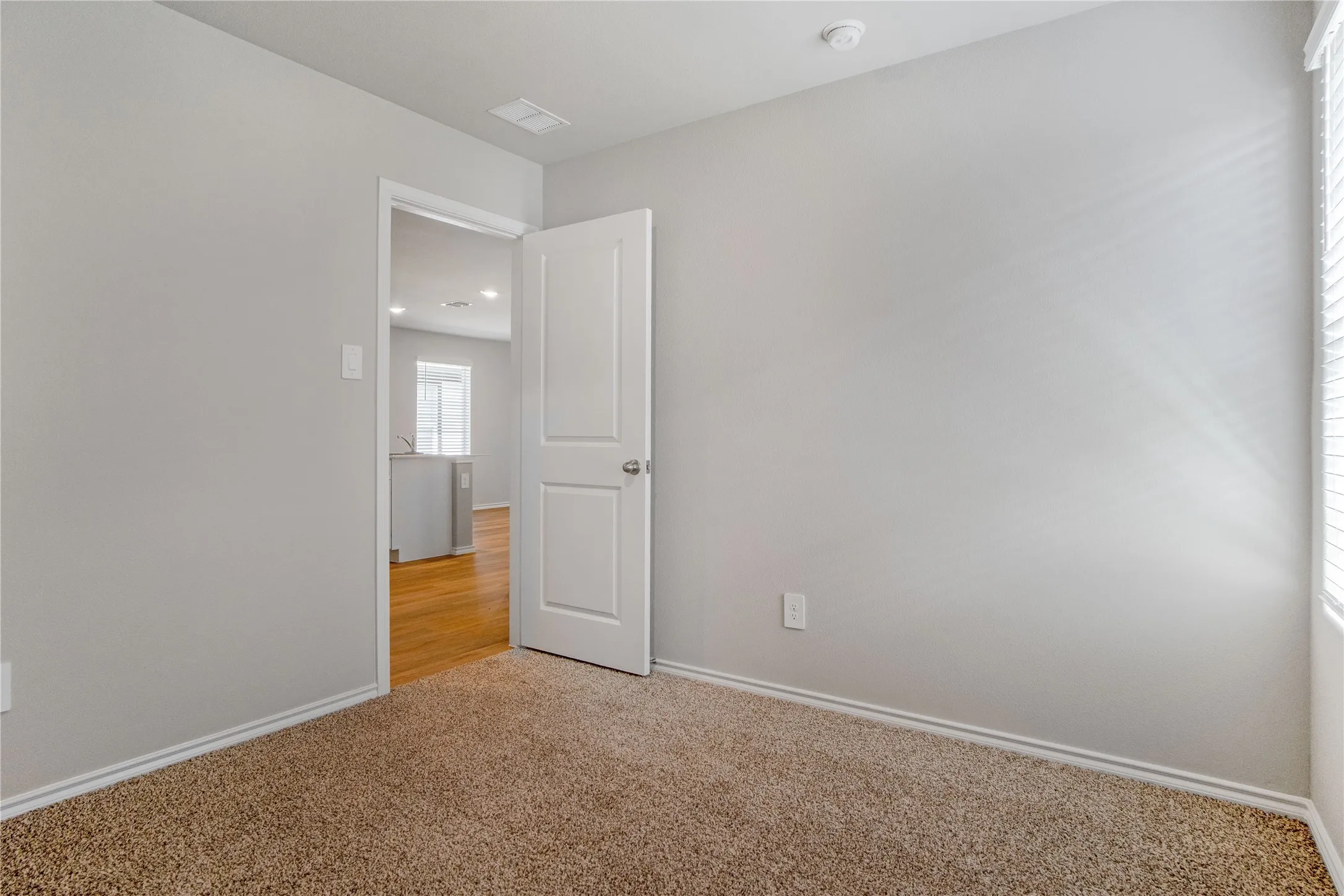 Neutral wall palette, neutral-toned carpeting, two-panel interior door, and window with integrated blinds