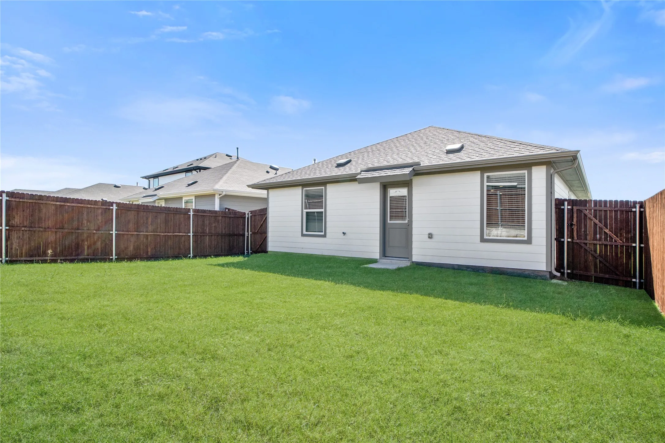 Fenced backyard featuring a manicured lawn, horizontal lap siding, and roof-integrated skylights