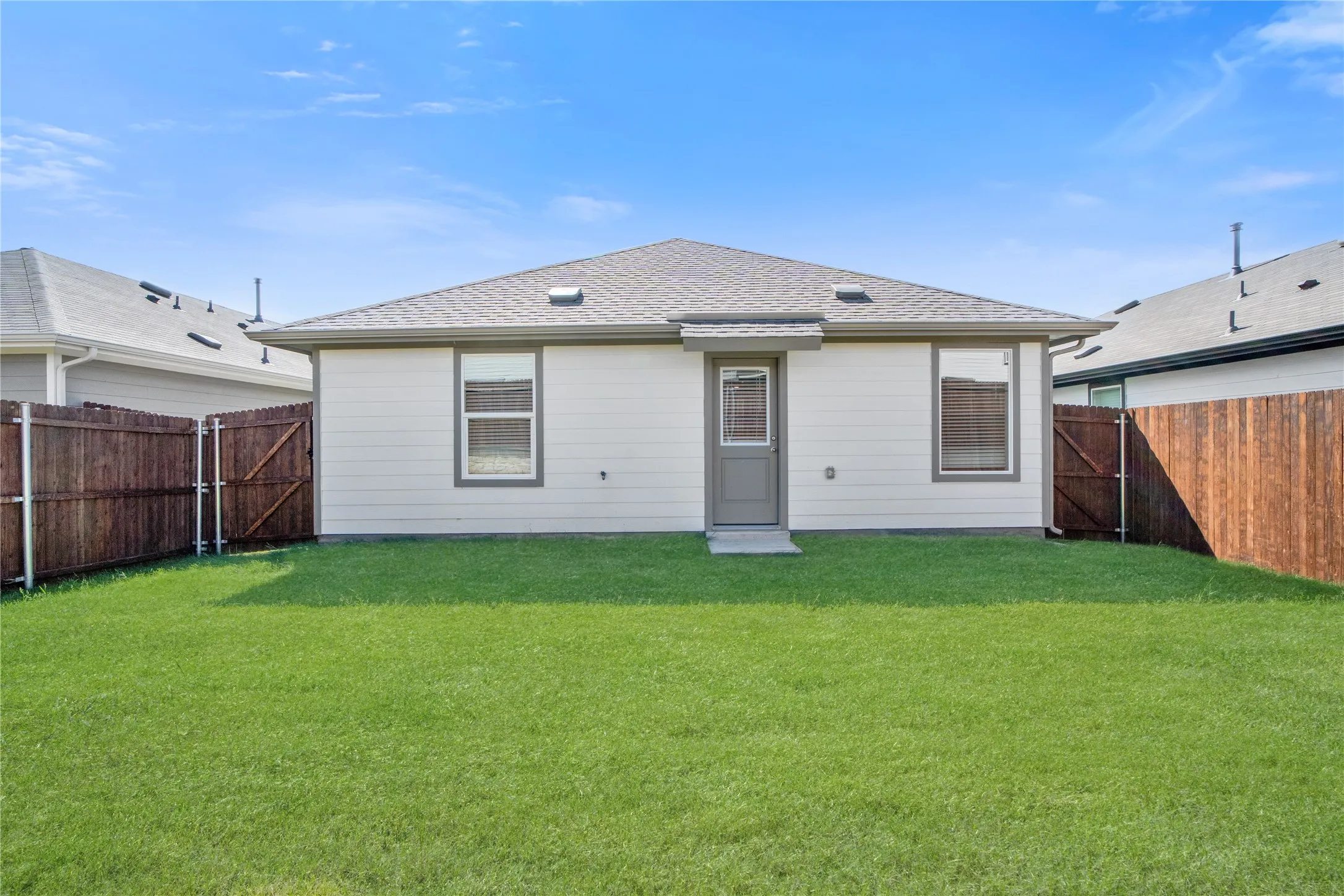 Rear exterior featuring horizontal lap siding, a shingled hipped roof, and a fenced backyard with a grass lawn