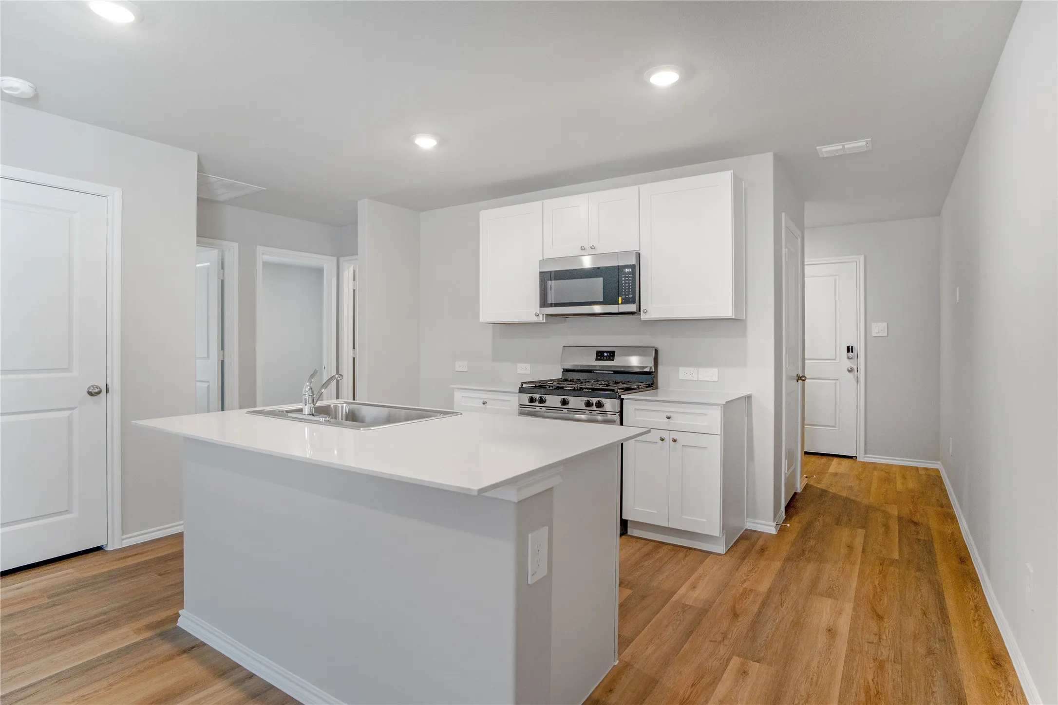 Kitchen featuring white cabinetry, an island with a stone countertop and undermount sink, stainless steel gas range, and wood-finish flooring