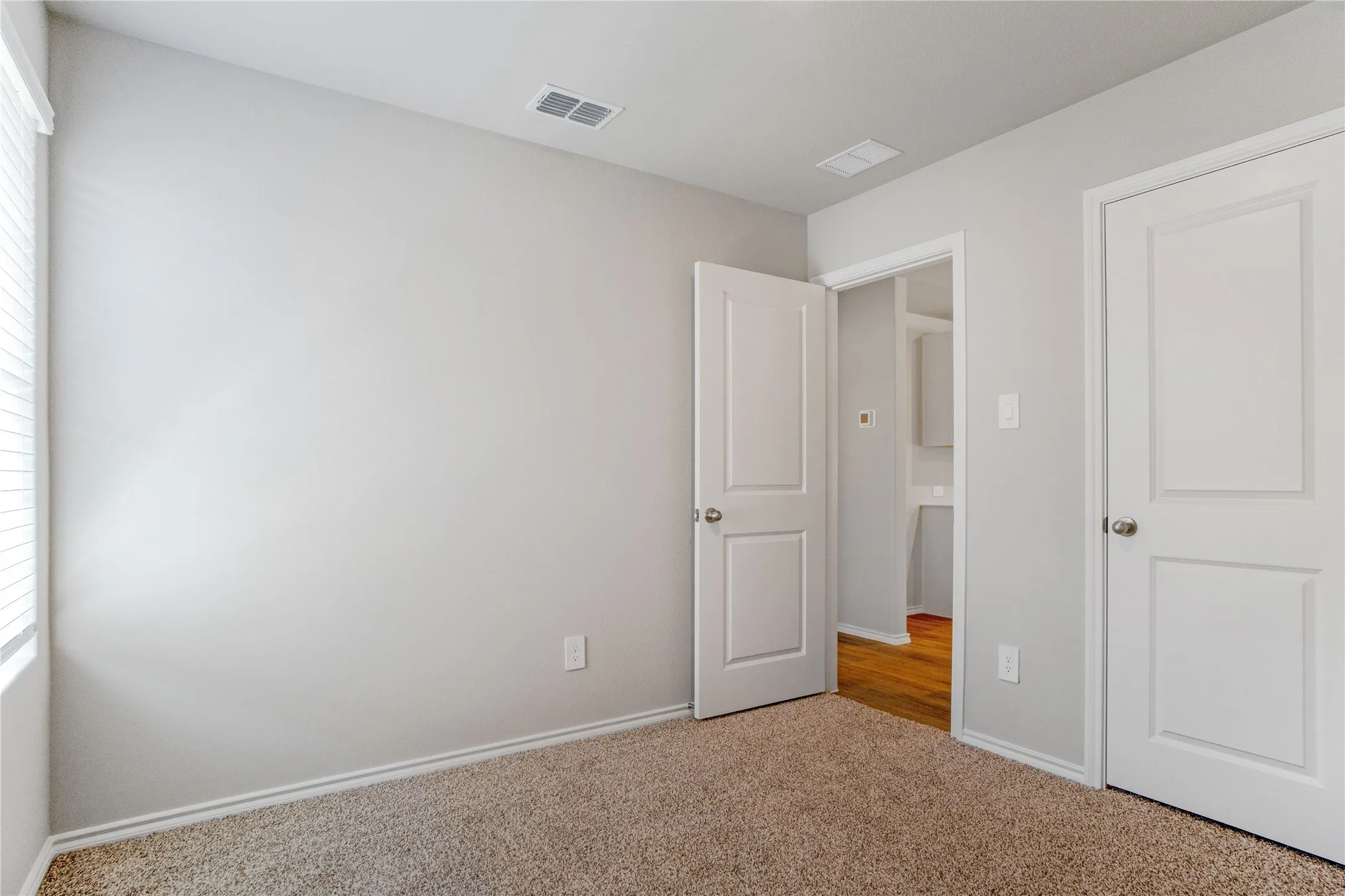 Neutral-toned interior space featuring wall-to-wall carpeting, white two-panel interior doors, and a window with horizontal blinds