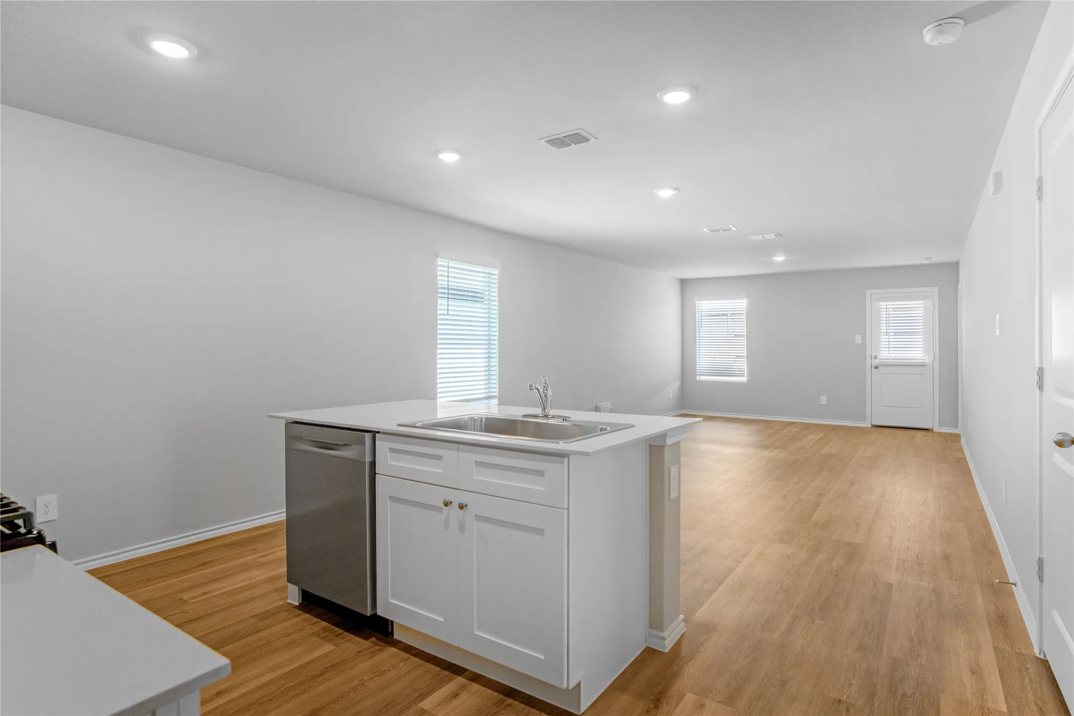Kitchen island with solid surface countertop, undermount stainless steel sink, integrated dishwasher, and wood-finish flooring illuminated by recessed lighting