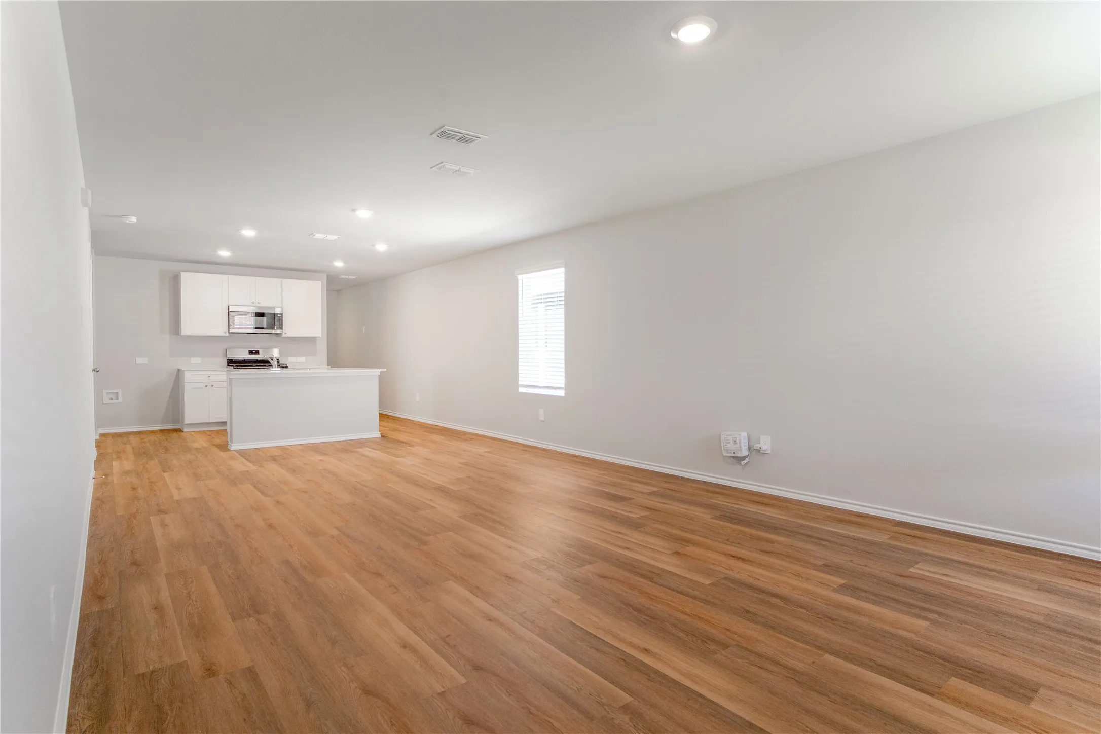 Open interior featuring wood-finish flooring, recessed lighting, and a kitchen with white cabinetry and a built-in peninsula