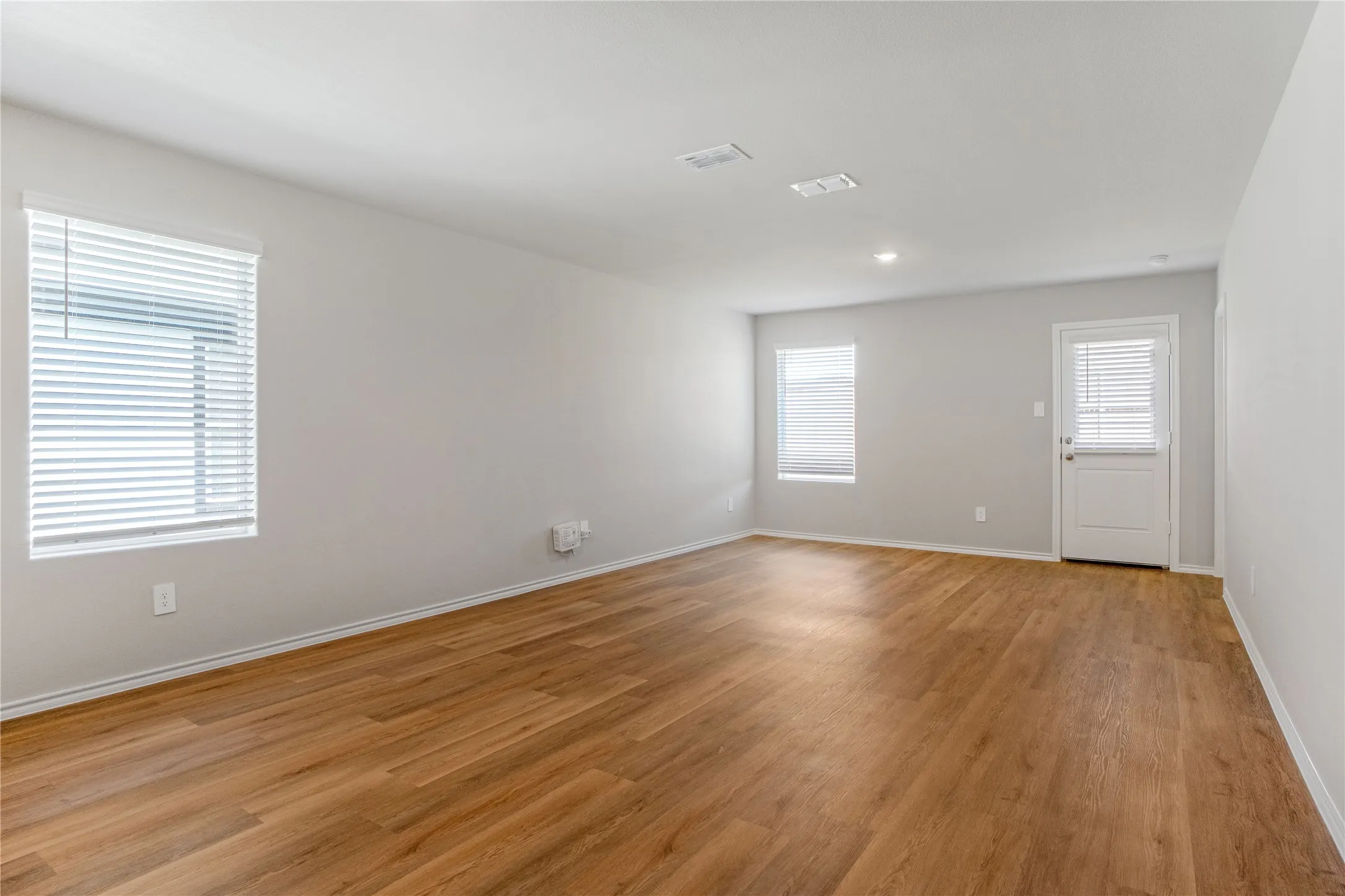 Interior space featuring wood-finish flooring, neutral wall tones, two windows with integrated blinds, and an exterior door
