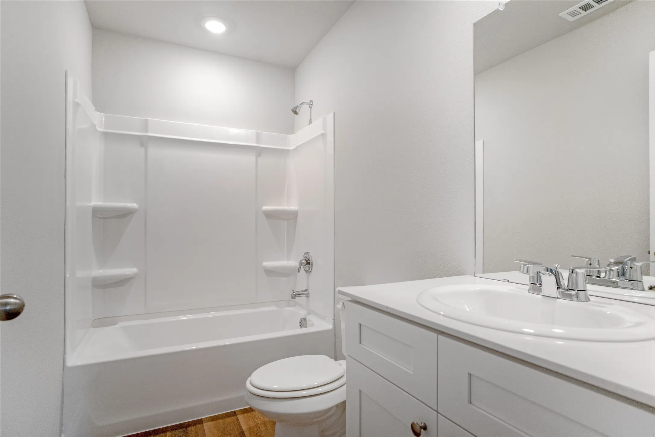 Bathroom featuring a white vanity cabinet, solid-surface countertop with an integrated basin, chrome-finish faucet, and a white acrylic tub-shower surround with built-in shelving