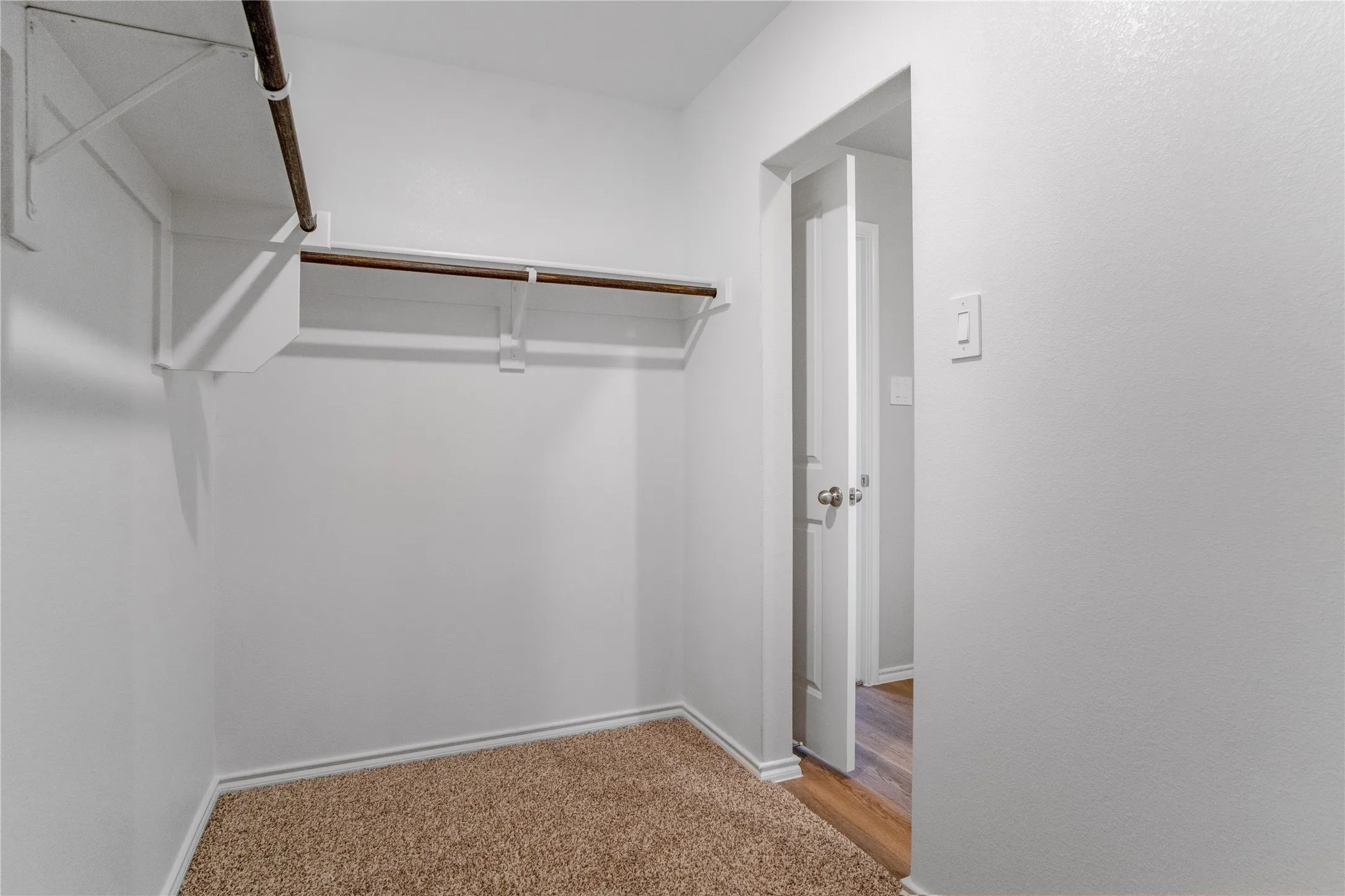 Storage area featuring neutral carpeting, white walls, and built-in white shelving with integrated garment rods