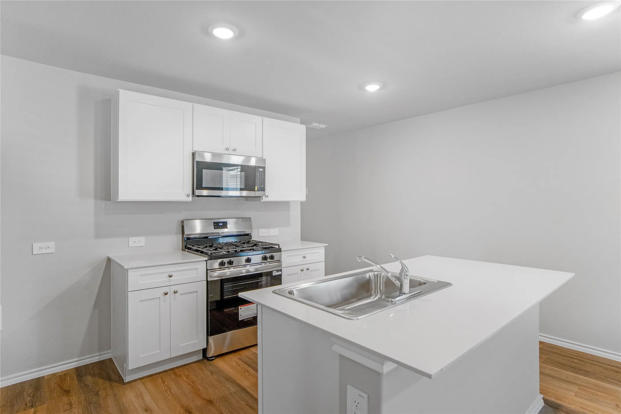Kitchen featuring white cabinetry, solid-surface countertops, stainless steel gas range, built-in microwave, and wood-finish flooring