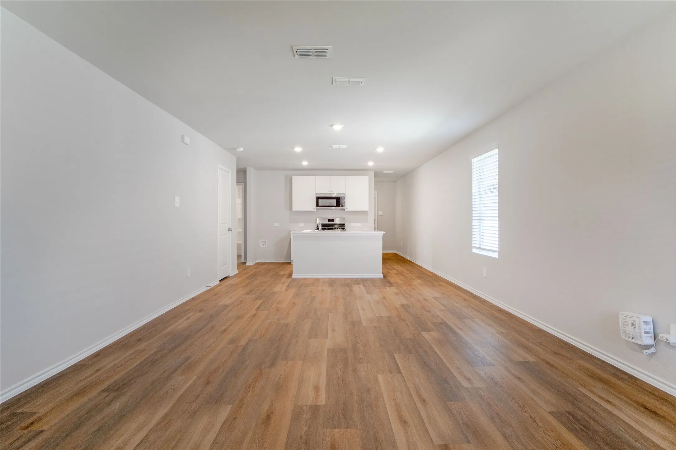 Open-concept interior featuring wood-finish flooring, recessed lighting, and a kitchen equipped with white cabinetry, a center island, and stainless steel appliances