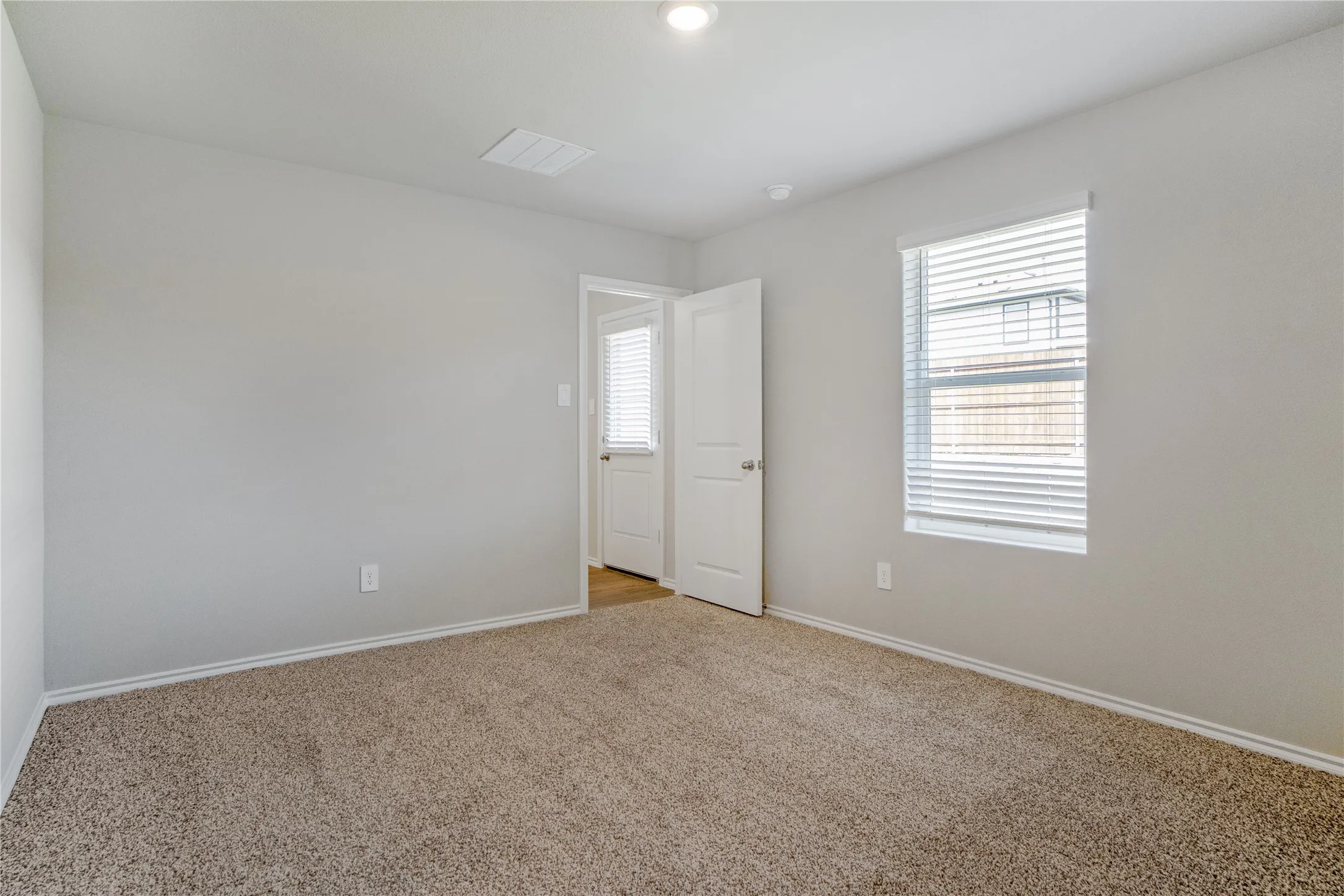 Neutral-toned interior space featuring wall-to-wall carpeting, recessed ceiling lighting, and a single-hung window with horizontal blinds