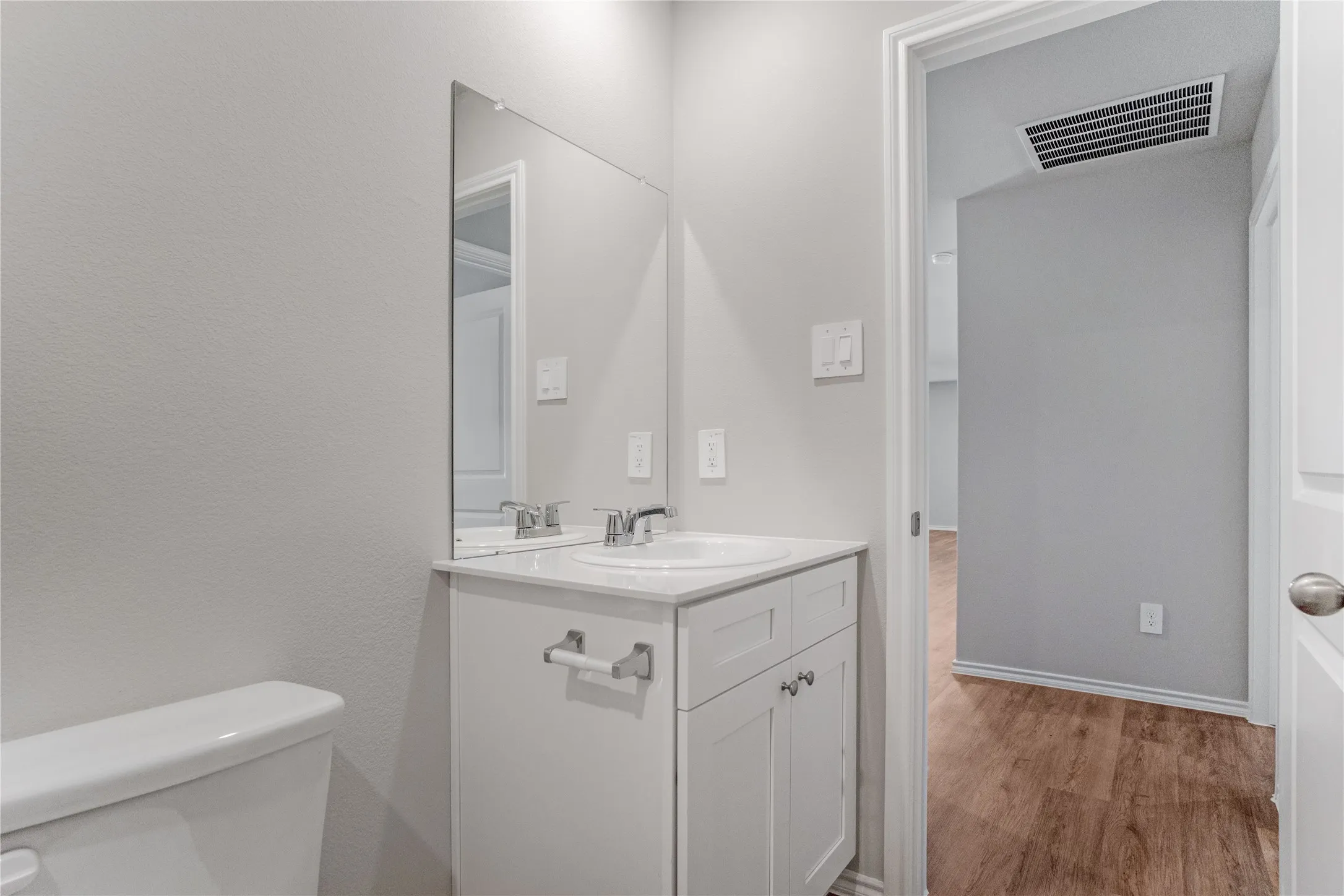 White cabinetry vanity with a stone-finish countertop, integrated basin, chrome finish faucet, and large wall-mounted mirror