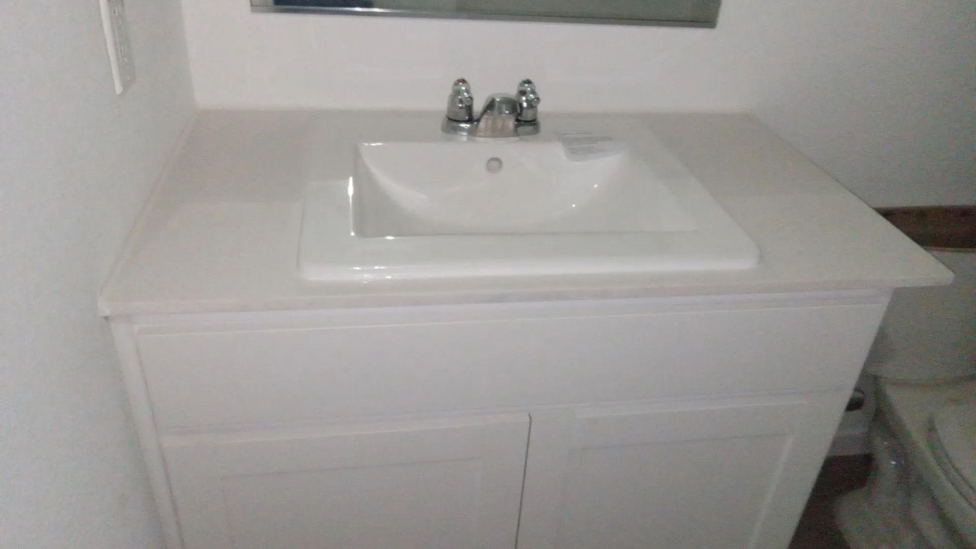White vanity cabinet featuring a solid-surface countertop with an integrated basin, chrome dual-handle faucet, and rectangular mirror