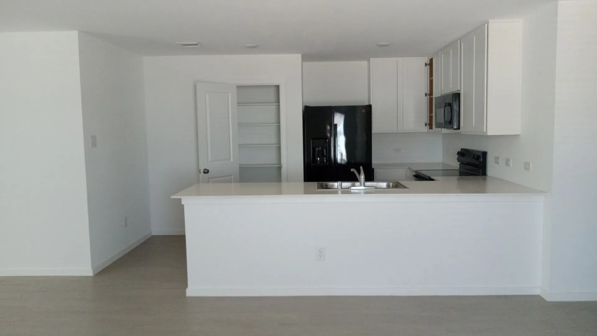 Kitchen featuring white cabinetry, solid-surface countertops, black appliances, a double-basin stainless steel sink, and a walk-in pantry