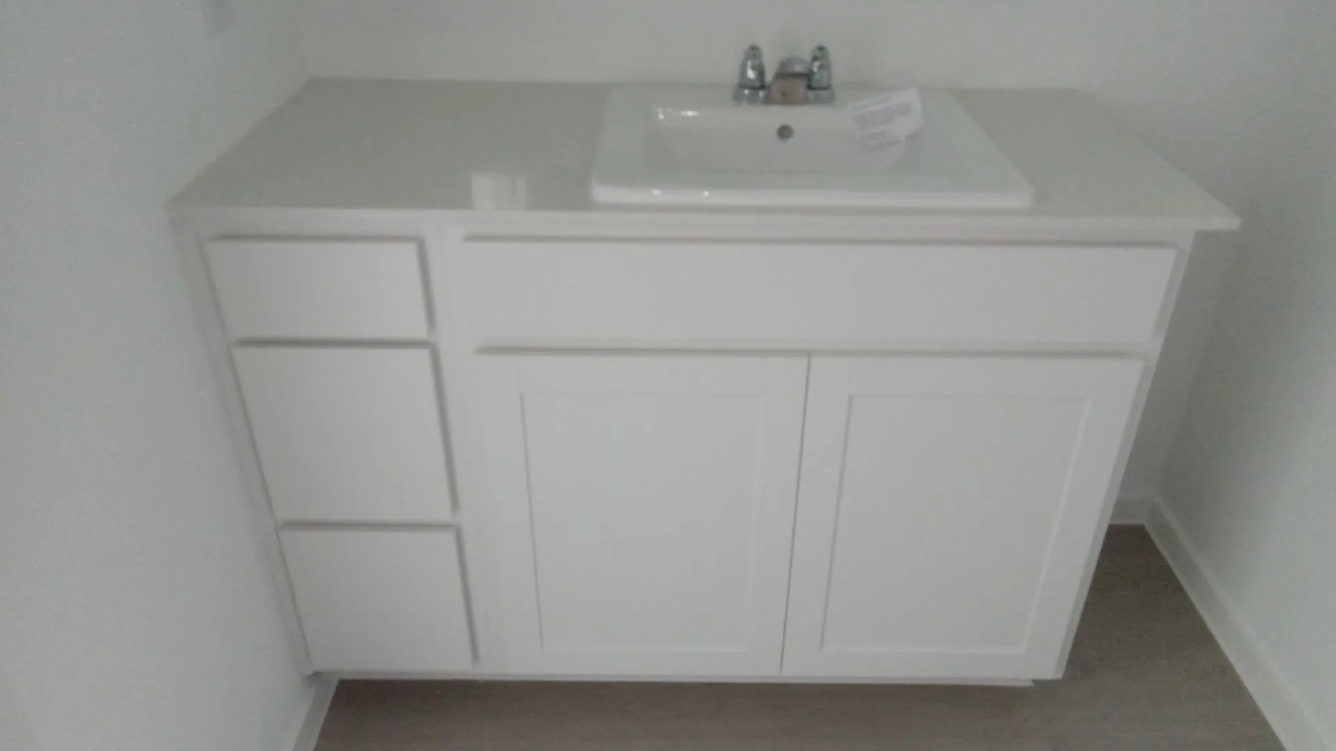 White cabinetry vanity featuring a stone-composite countertop, integrated drop-in sink, metallic dual-handle faucet, and three-drawer storage stack