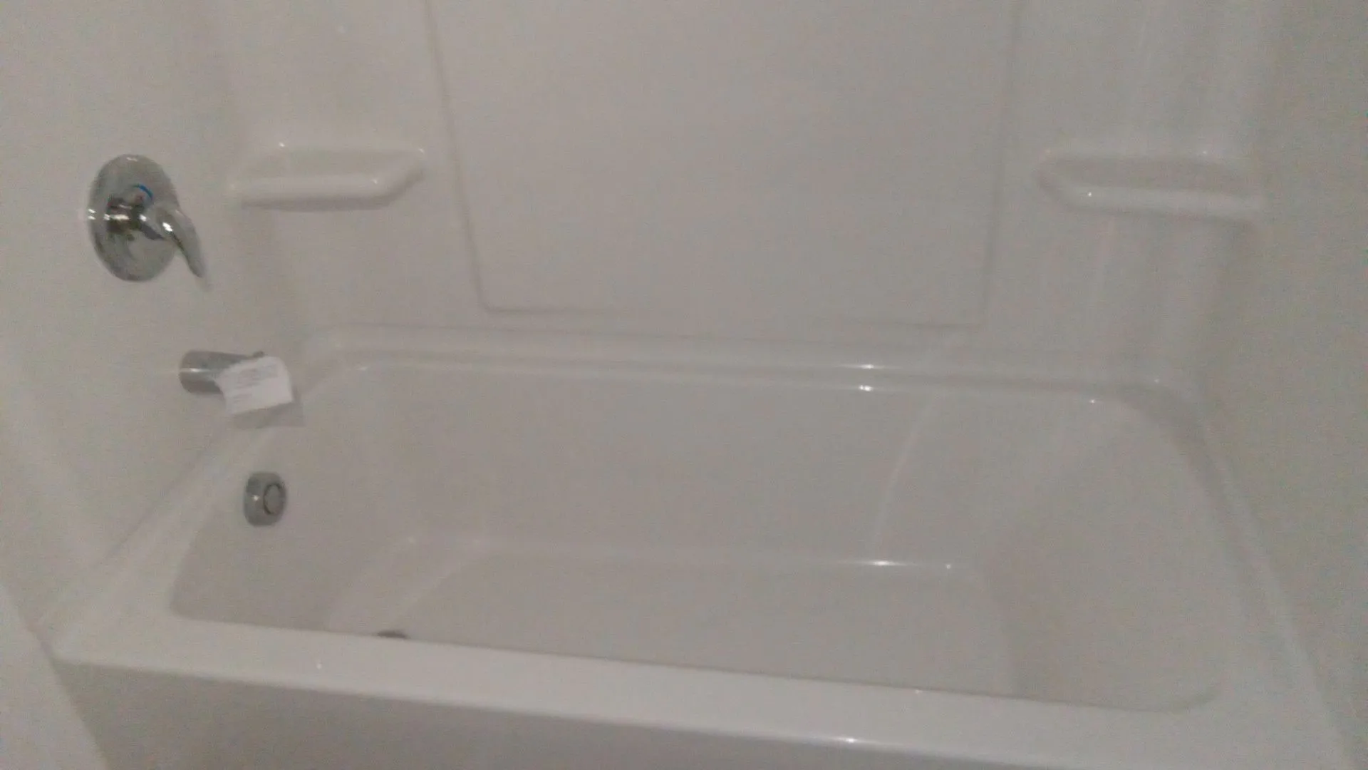 Bathtub featuring a white molded surround with integrated shelving and a chrome-finish single-handle mixing valve