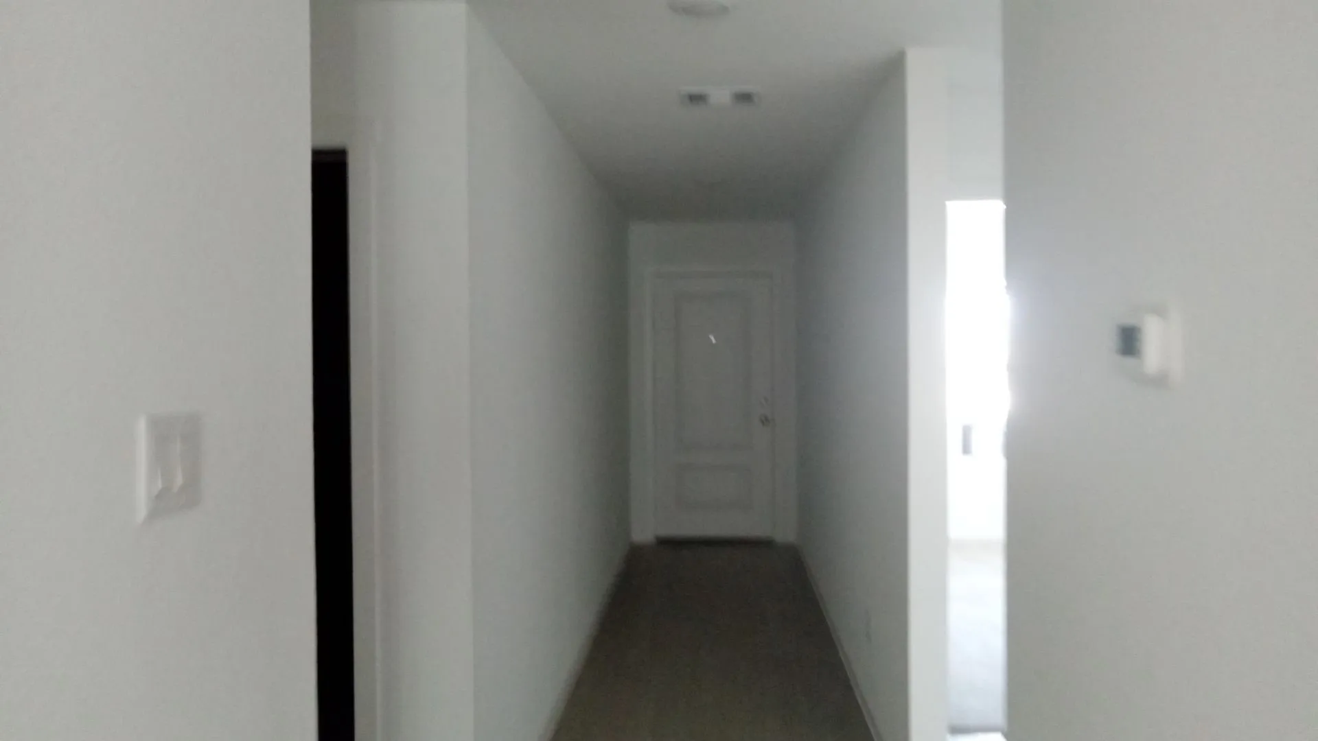 Hallway featuring wood-finish flooring, a solid core interior door, and wall-mounted climate control interface