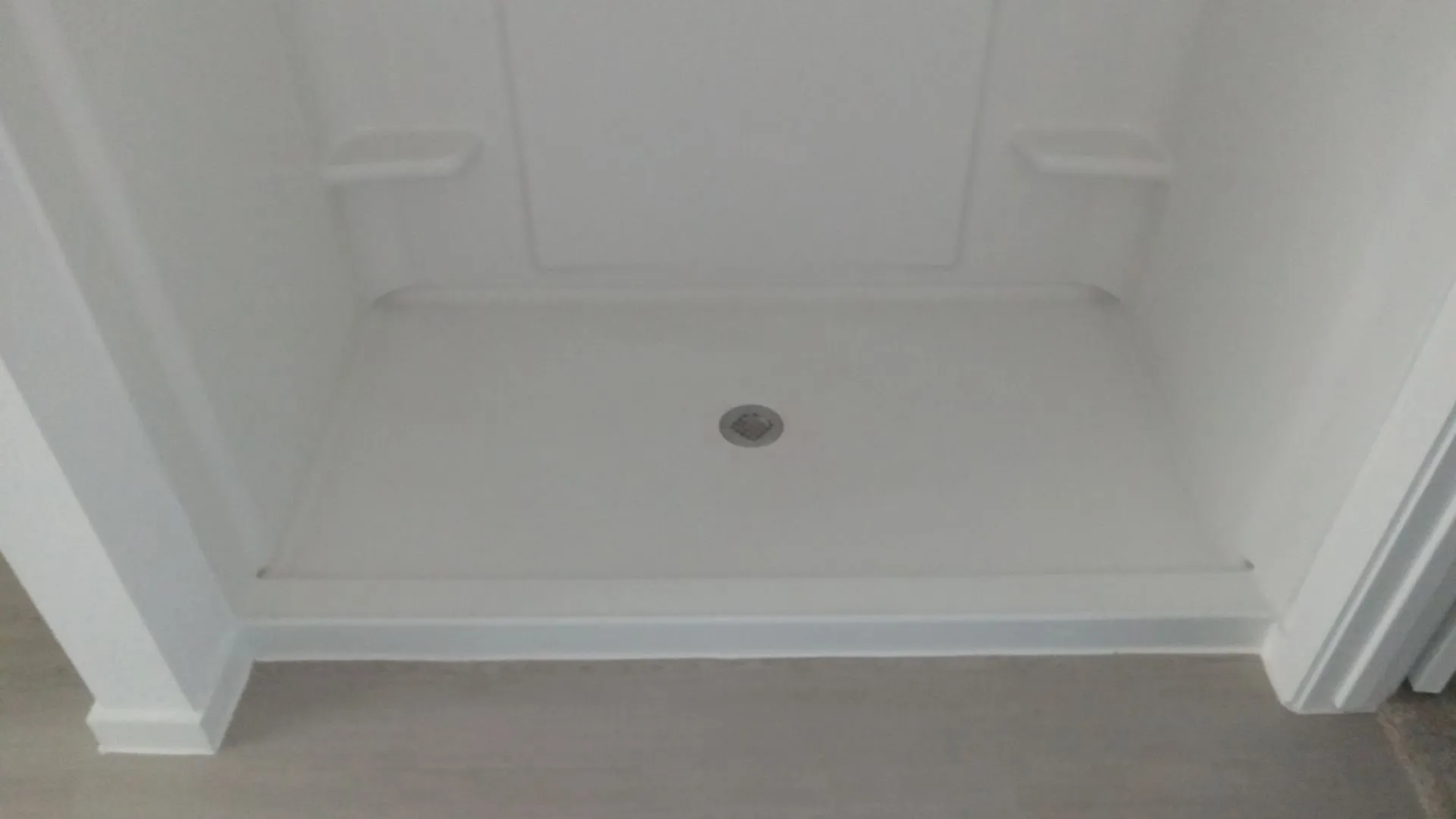 Walk-in shower enclosure featuring a white surround, integrated shelving, and a low-threshold base