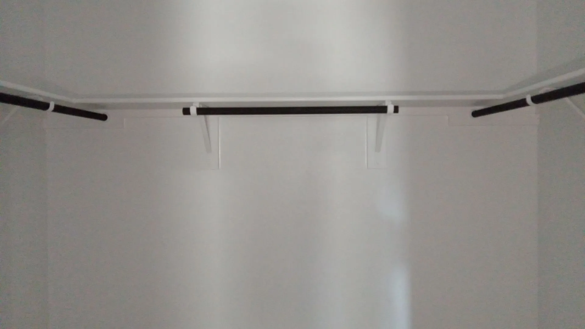 Walk-in closet featuring white wood shelving and matte black hanging rods
