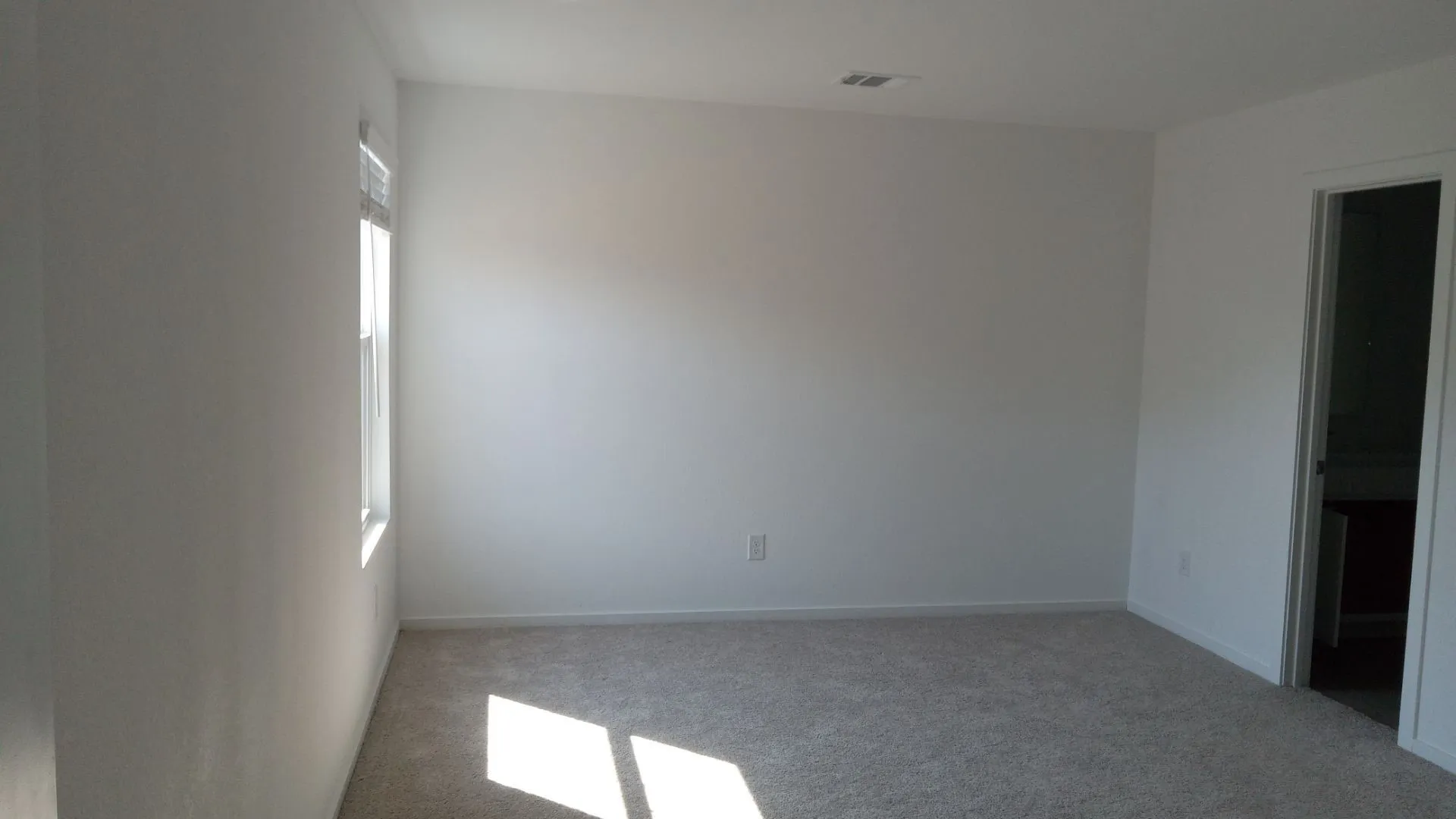 Neutral-toned walls, plush wall-to-wall carpeting, and natural light provided by a single window with fitted blinds