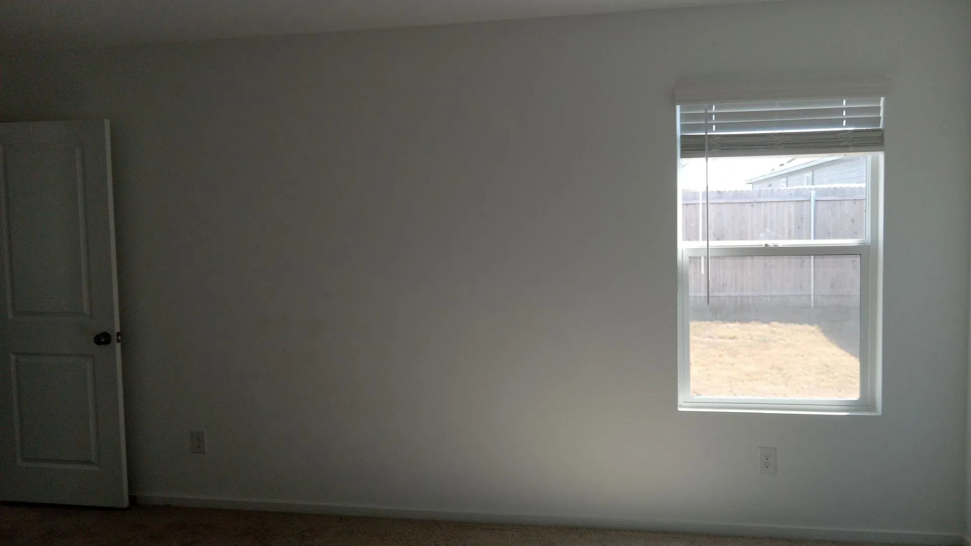 Neutral-toned walls, carpeted flooring, single-panel interior door with a round knob, and a window featuring horizontal blinds
