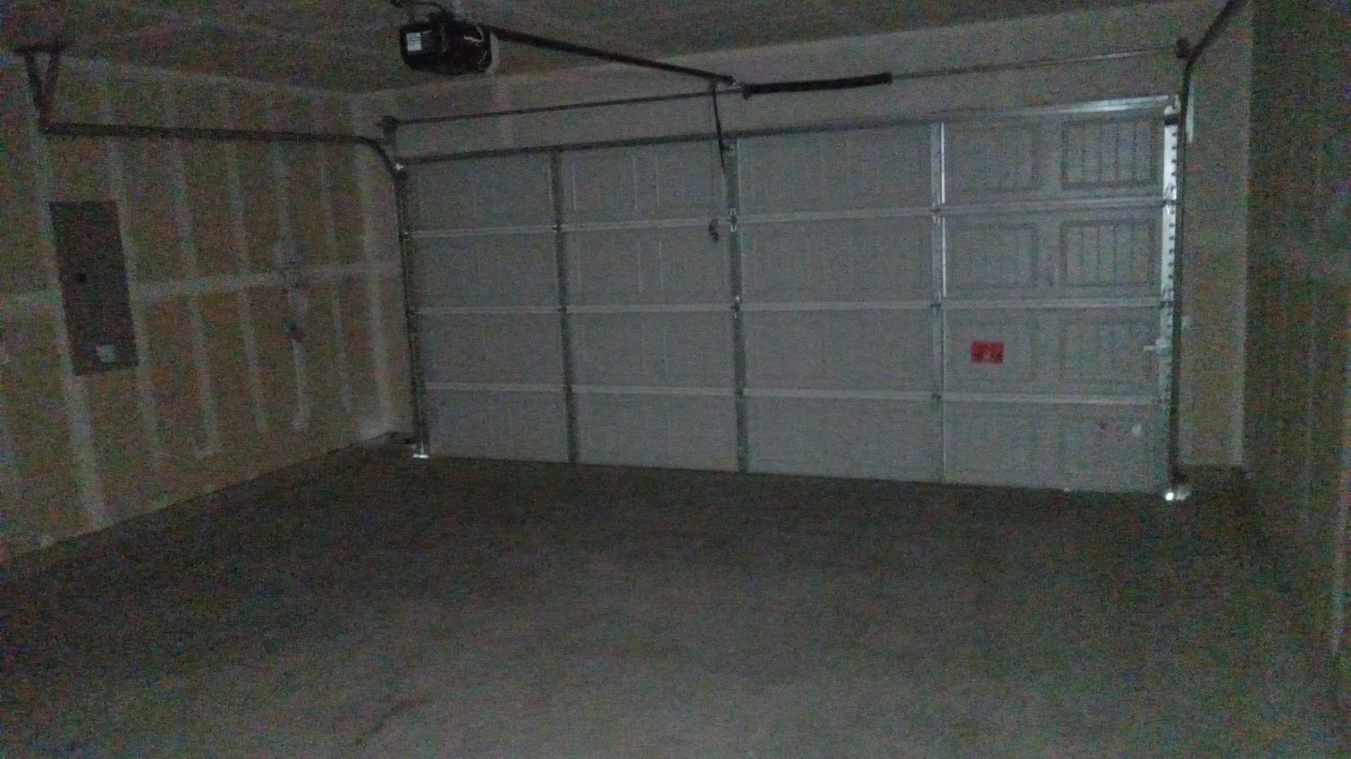 Two-car garage featuring a sectional overhead door, automated door opener, concrete flooring, and unfinished drywall