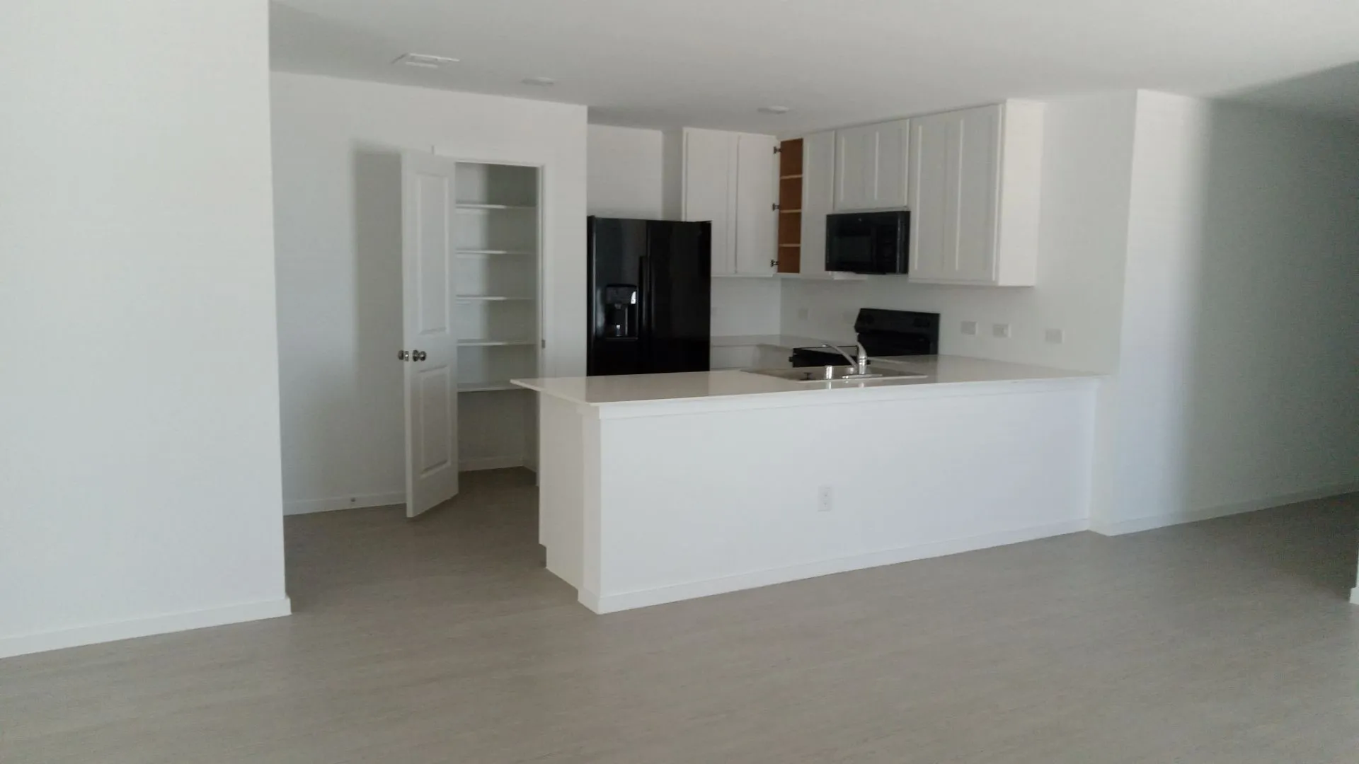 Kitchen featuring white shaker-style cabinetry, quartz countertops, a peninsula with a stainless steel sink, black appliances, and a built-in pantry with shelving