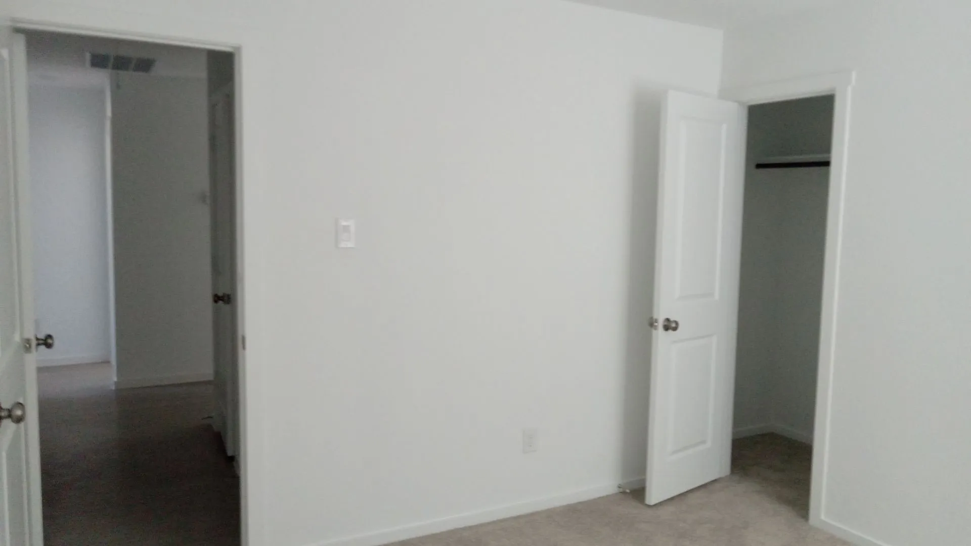Interior space featuring neutral wall paint, carpeted flooring, and white paneled doors with metallic hardware