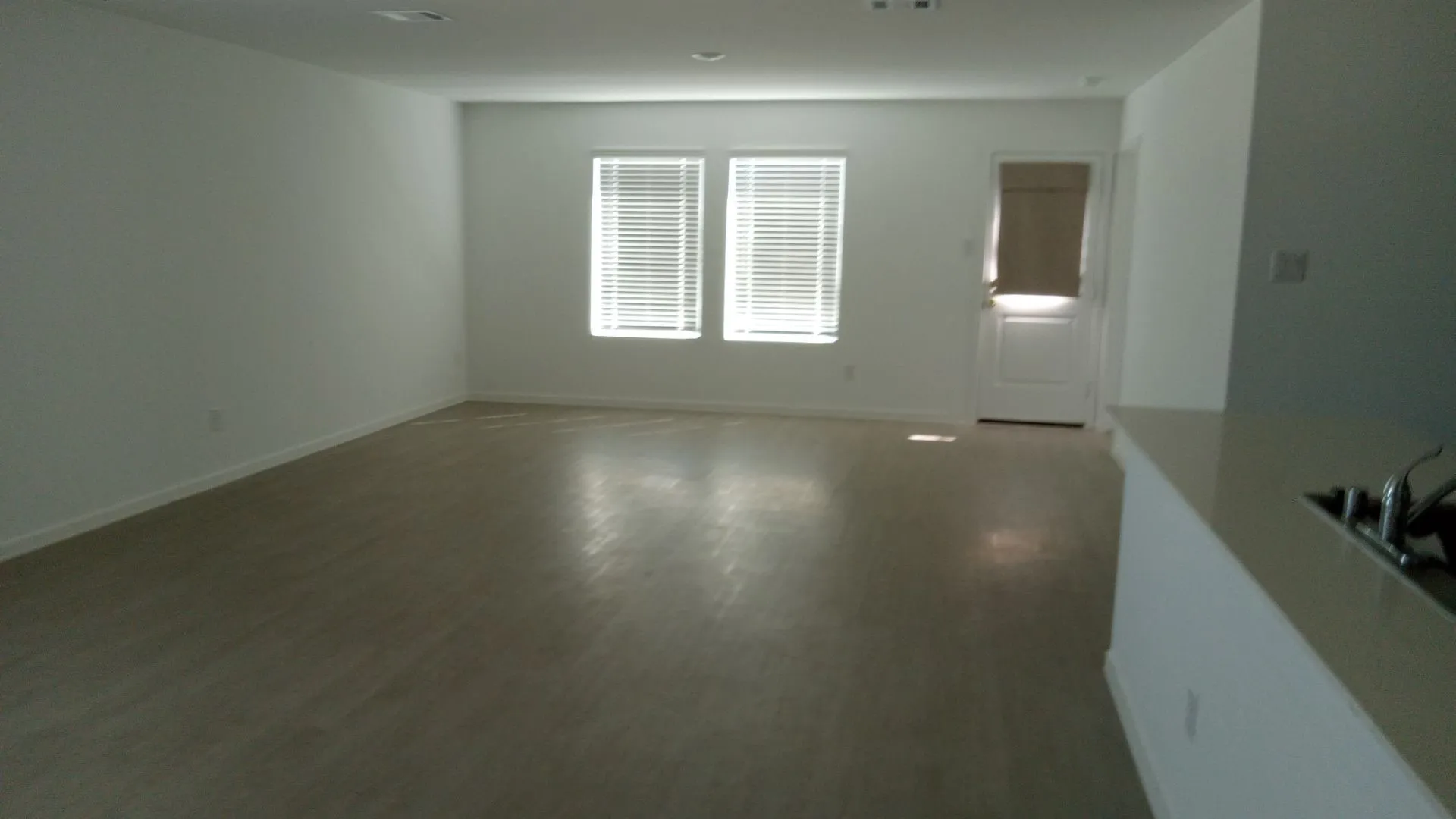 Open-concept room featuring light-toned wood-finish flooring, recessed lighting, and dual windows with fitted blinds