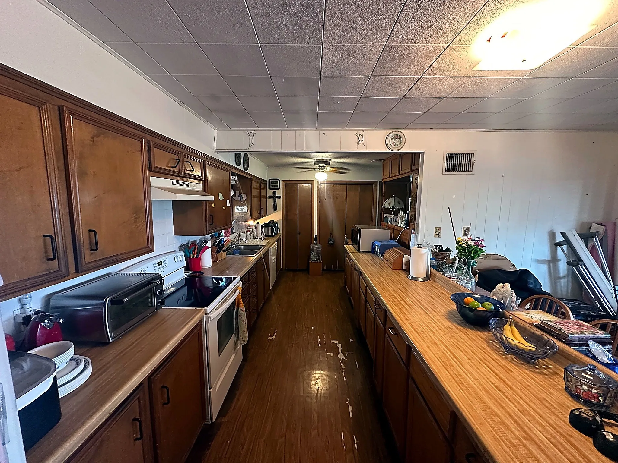 Galley kitchen featuring wood cabinetry, laminate countertops, integrated range, and wood-finish flooring
