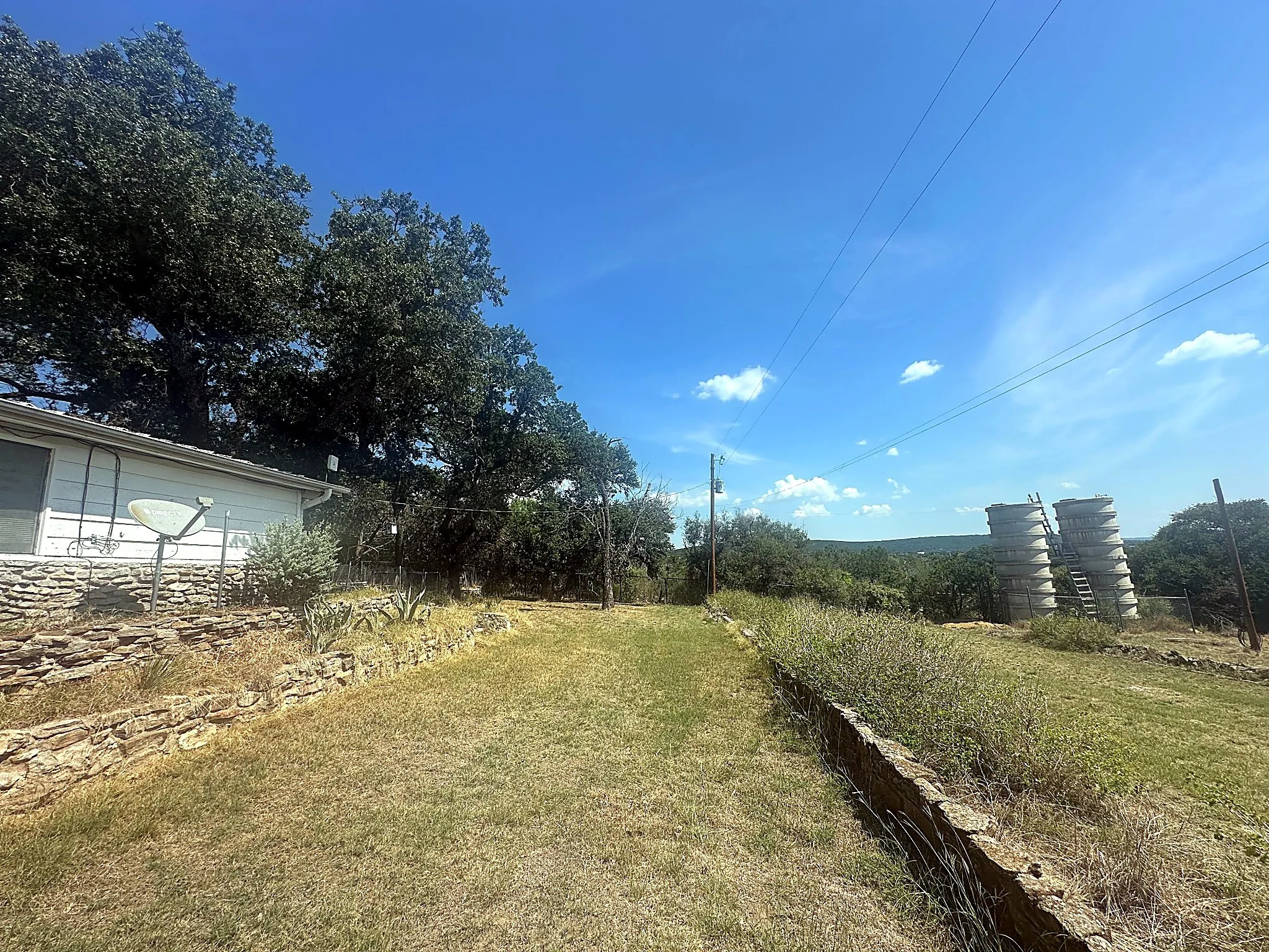 Expansive grounds featuring natural stone retaining walls, mature oak trees, and industrial storage silos