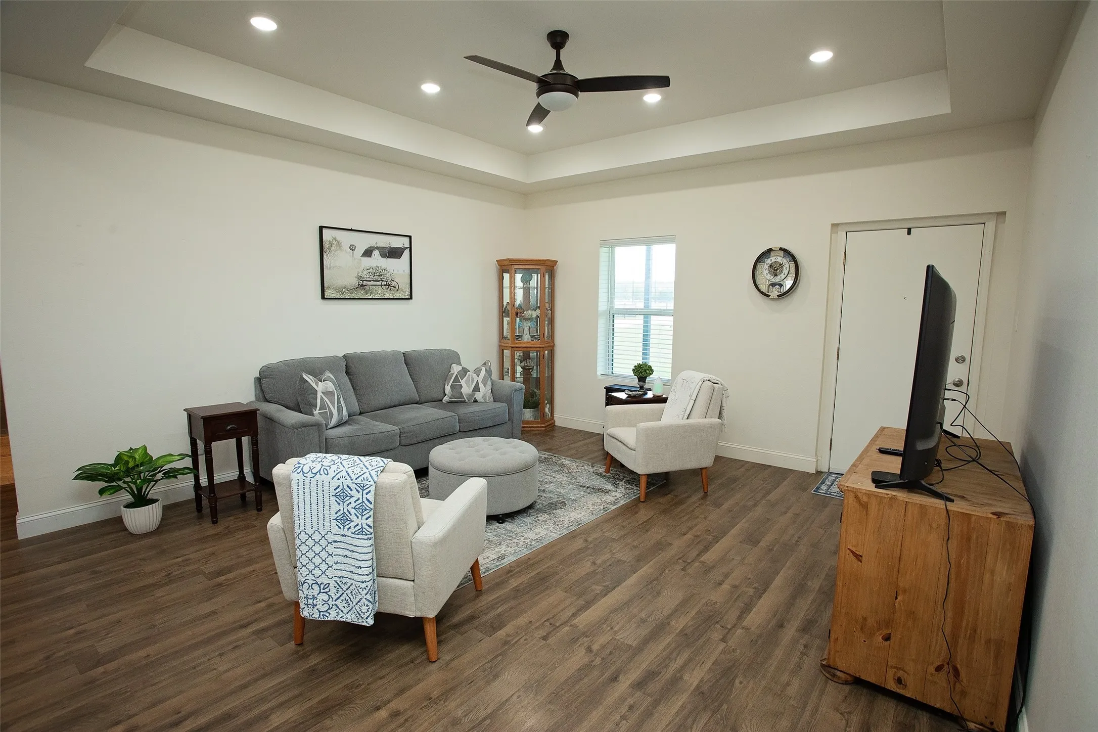 Tray ceiling with recessed lighting, central ceiling fan, and wood-finish flooring