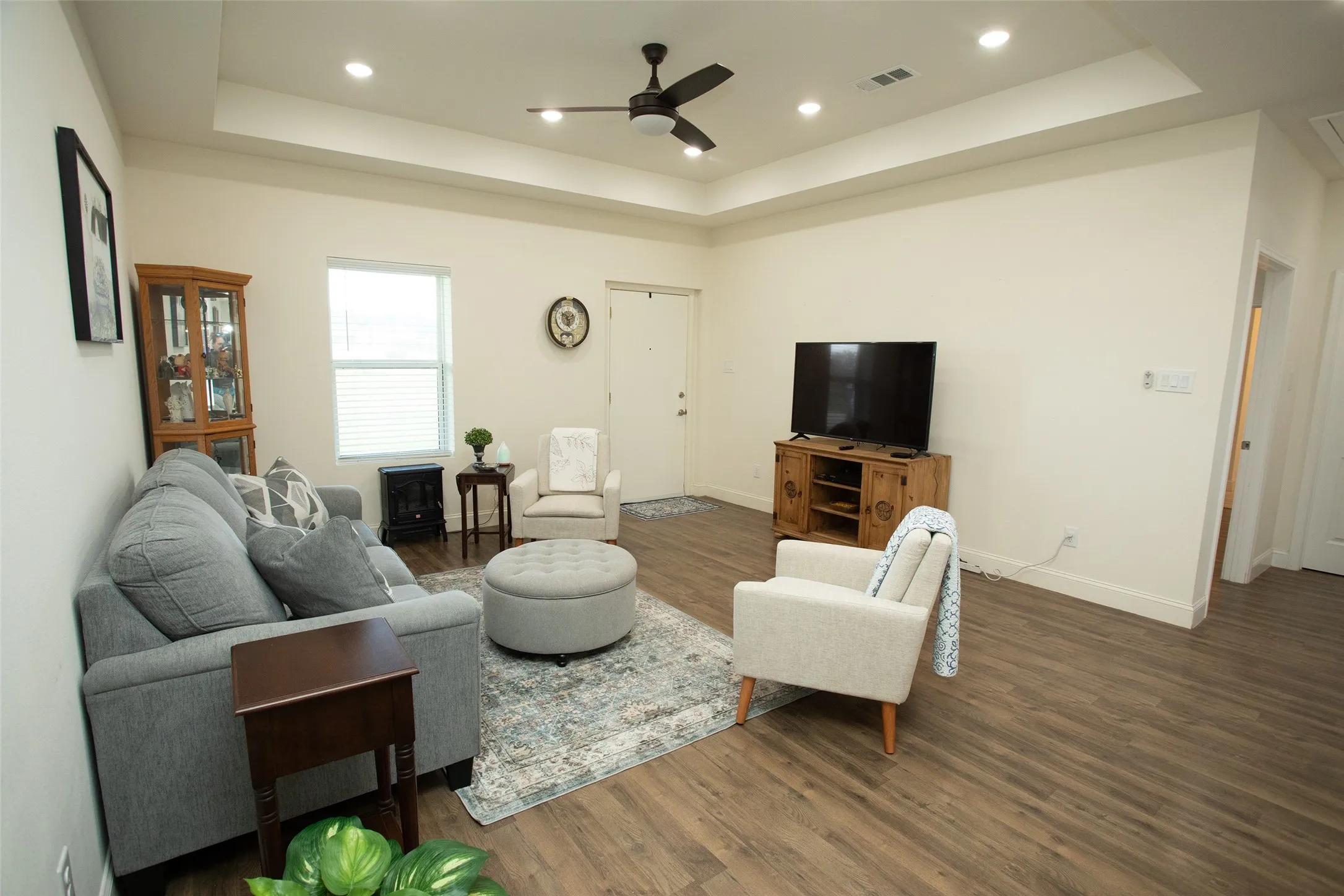 Tray ceiling featuring recessed lighting and a central ceiling fan, complemented by wood-finish flooring