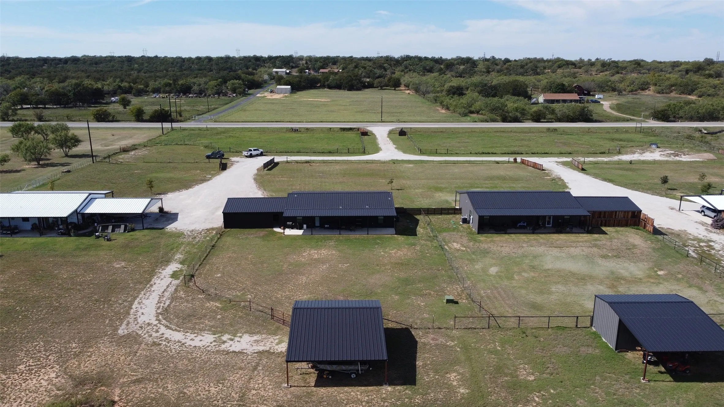 Aerial perspective of a multi-structure property featuring metal-roofed buildings, detached carports, fenced grounds, and expansive acreage