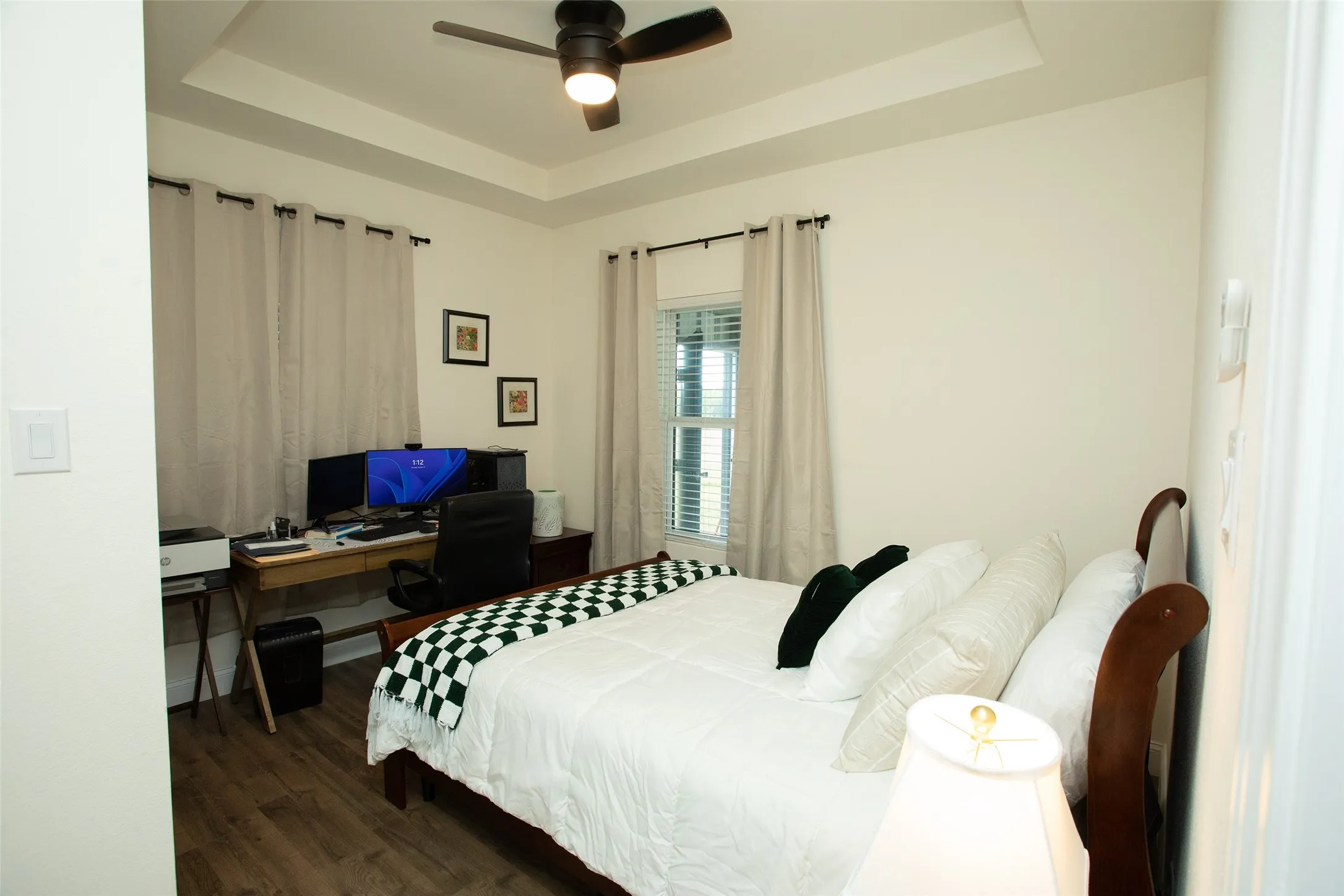 Room interior featuring a tray ceiling, wood-finish flooring, and a modern ceiling fan with integrated lighting